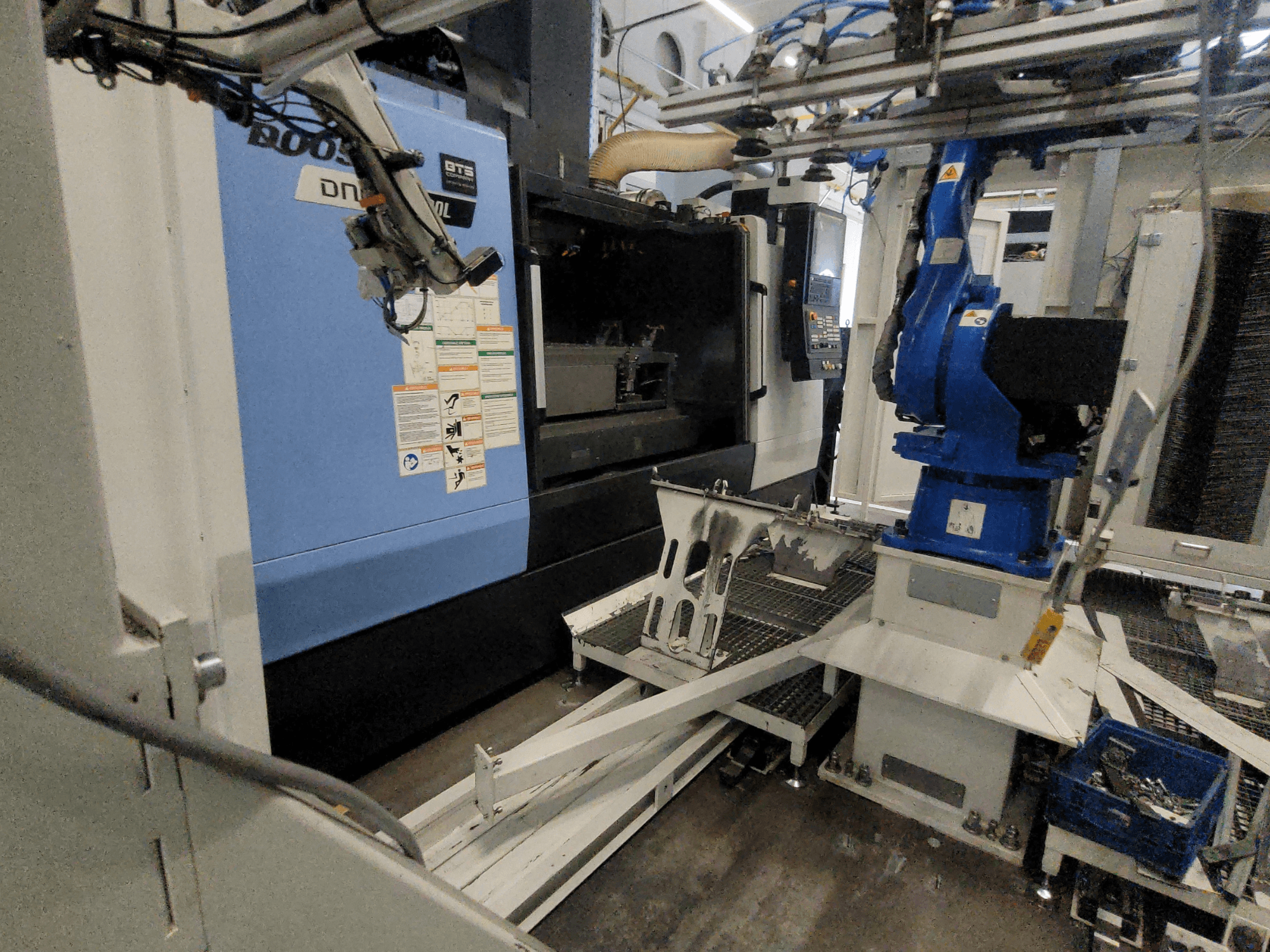 Vue latérale du centre d'usinage vertical DOOSAN DNM 6700L, avec le bras robotisé et le panneau de commande visibles, illustrant la configuration de la machine.