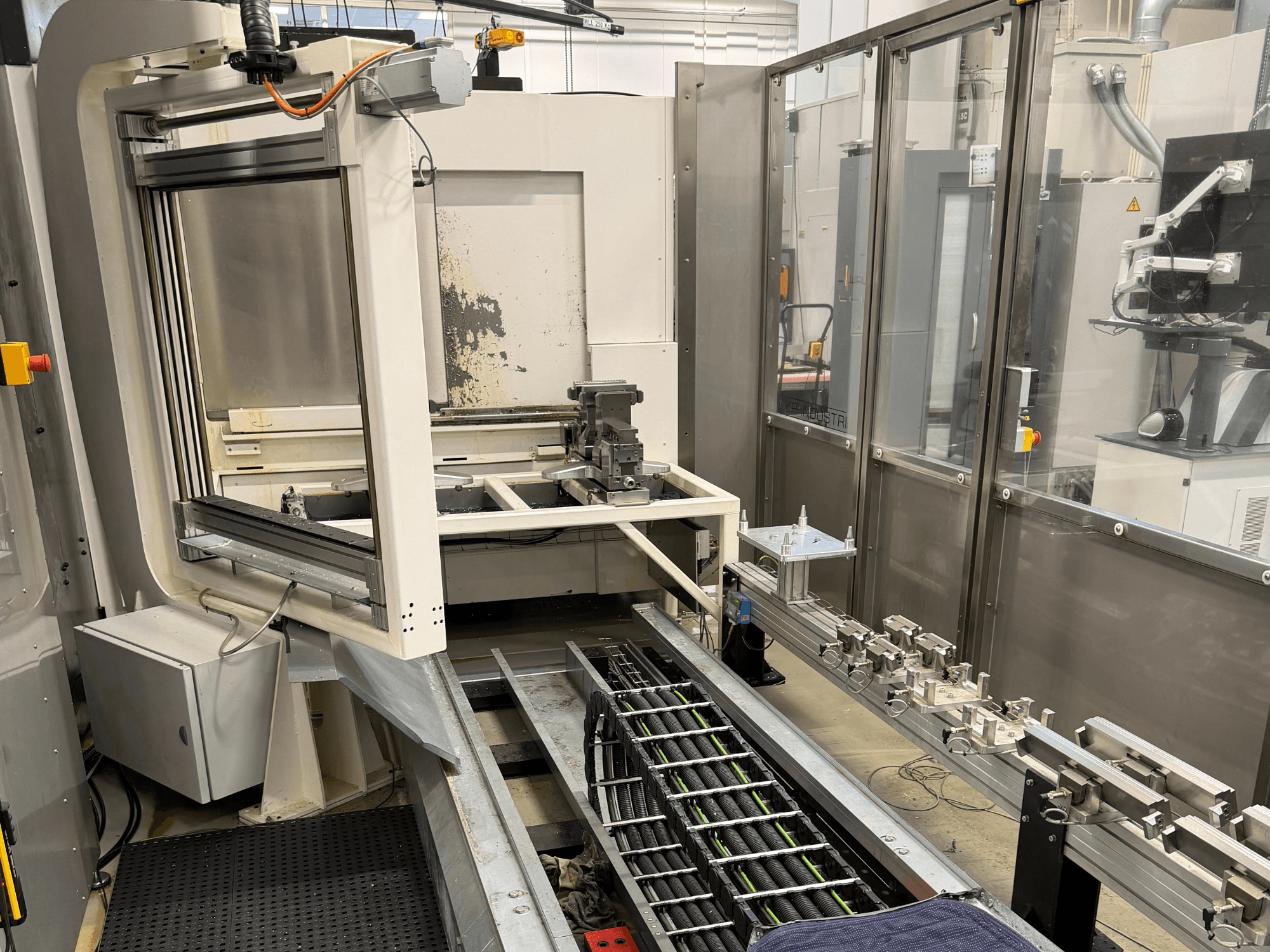 Poste de travail industriel automatisé présentant un bras robotisé, un système de rails et un panneau de commande en vue latérale.