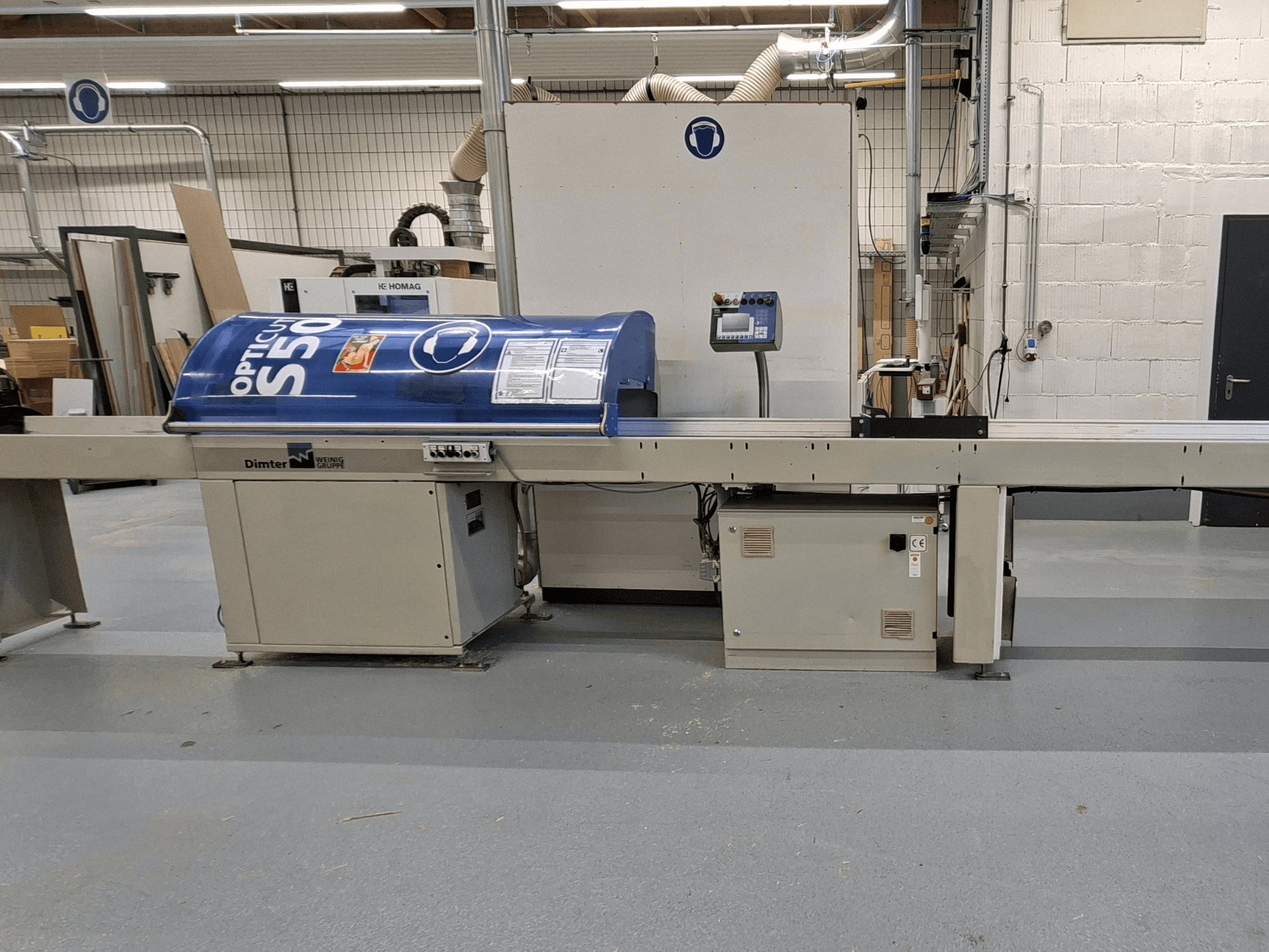 Machine à découper le bois Dimter OptiCut S50 vue de côté, avec un boîtier bleu, un panneau de commande et une bande transporteuse.