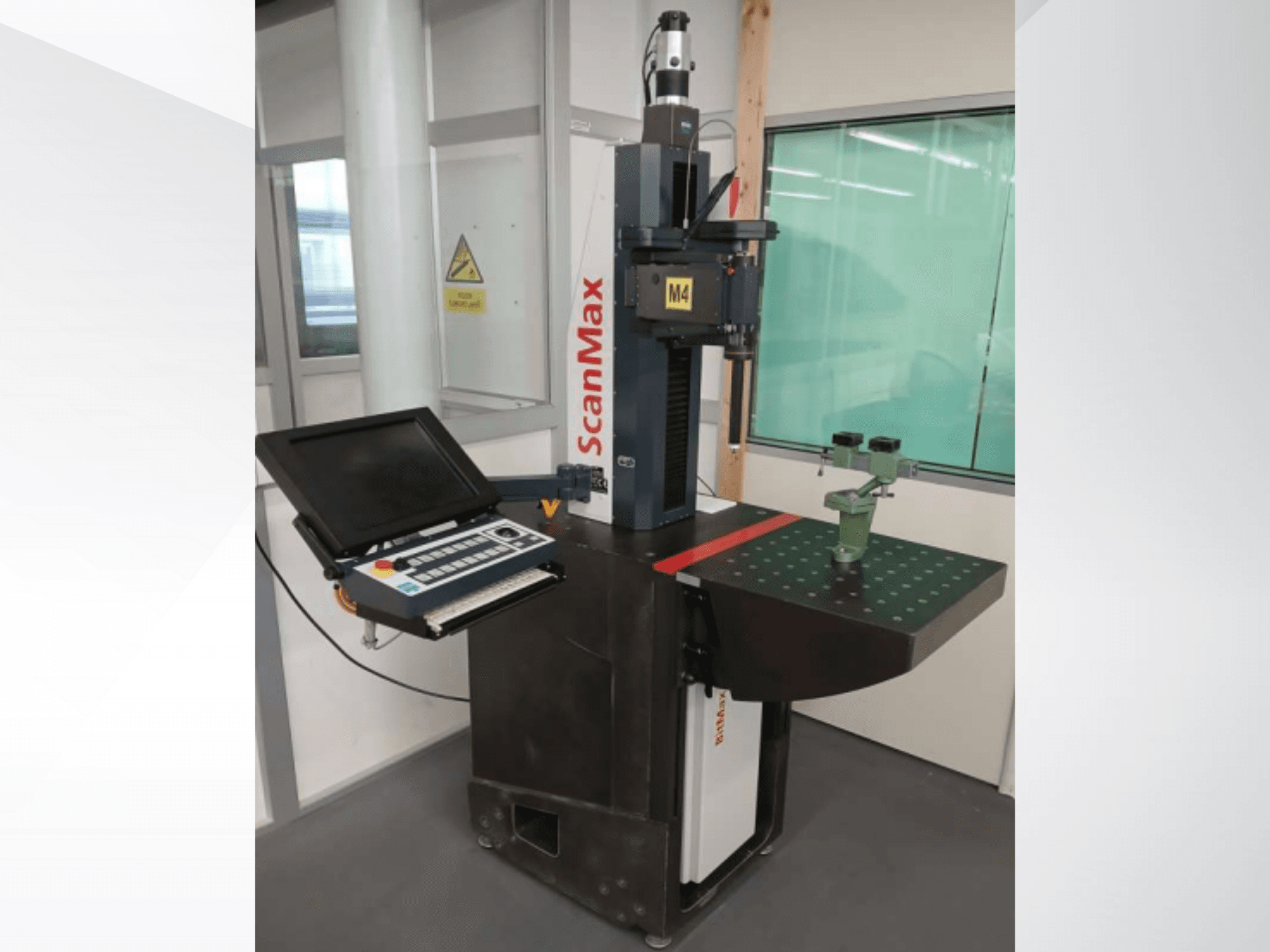 Machine de mesure ScanMax M4, vue de face avec le panneau de commande et le dispositif d'étalonnage vert sur une table de travail en pointillés.