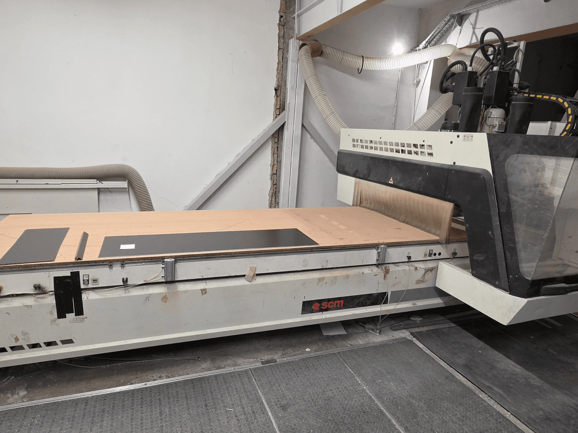 Centre d'usinage CNC SCM RECORD 132 vu de profil, doté d'une table de travail plane sur laquelle reposent des pièces noires et d'un système de dépoussiérage.