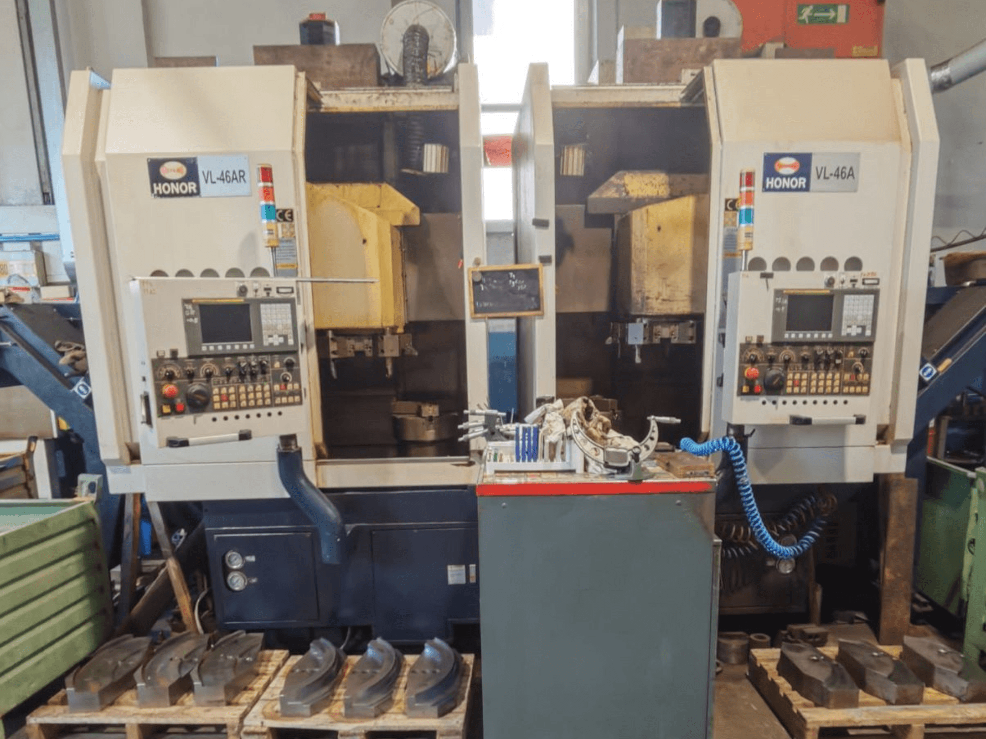 Vue de face du tour vertical HONOR SEIKI VL 46A, montrant le panneau de commande et les pièces environnantes posées sur des palettes en bois.