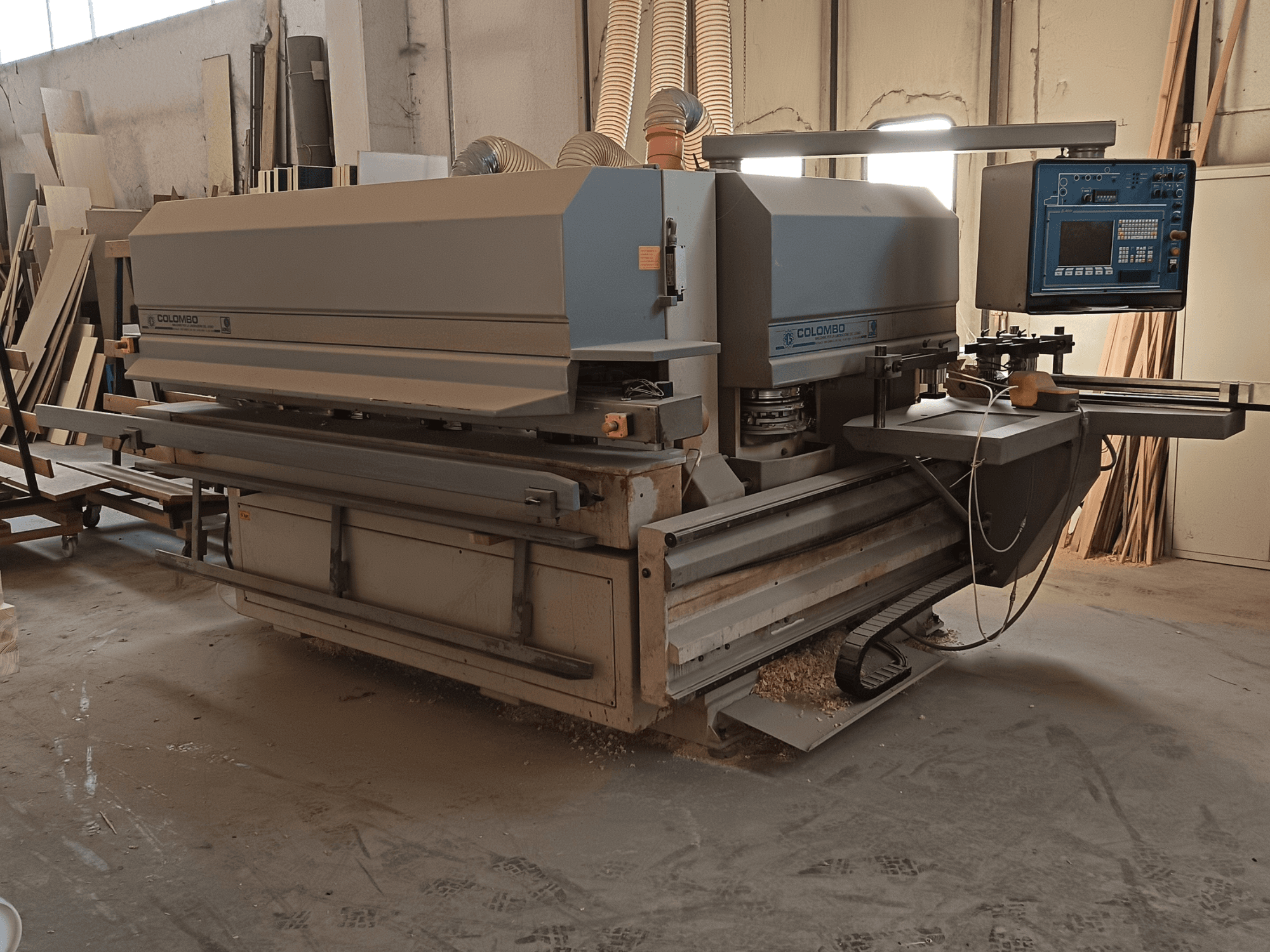 Machine à travailler le bois Colombo, vue de côté, montrant le panneau de commande, les lames de coupe et l'accumulation de poussière de scie dans l'atelier.