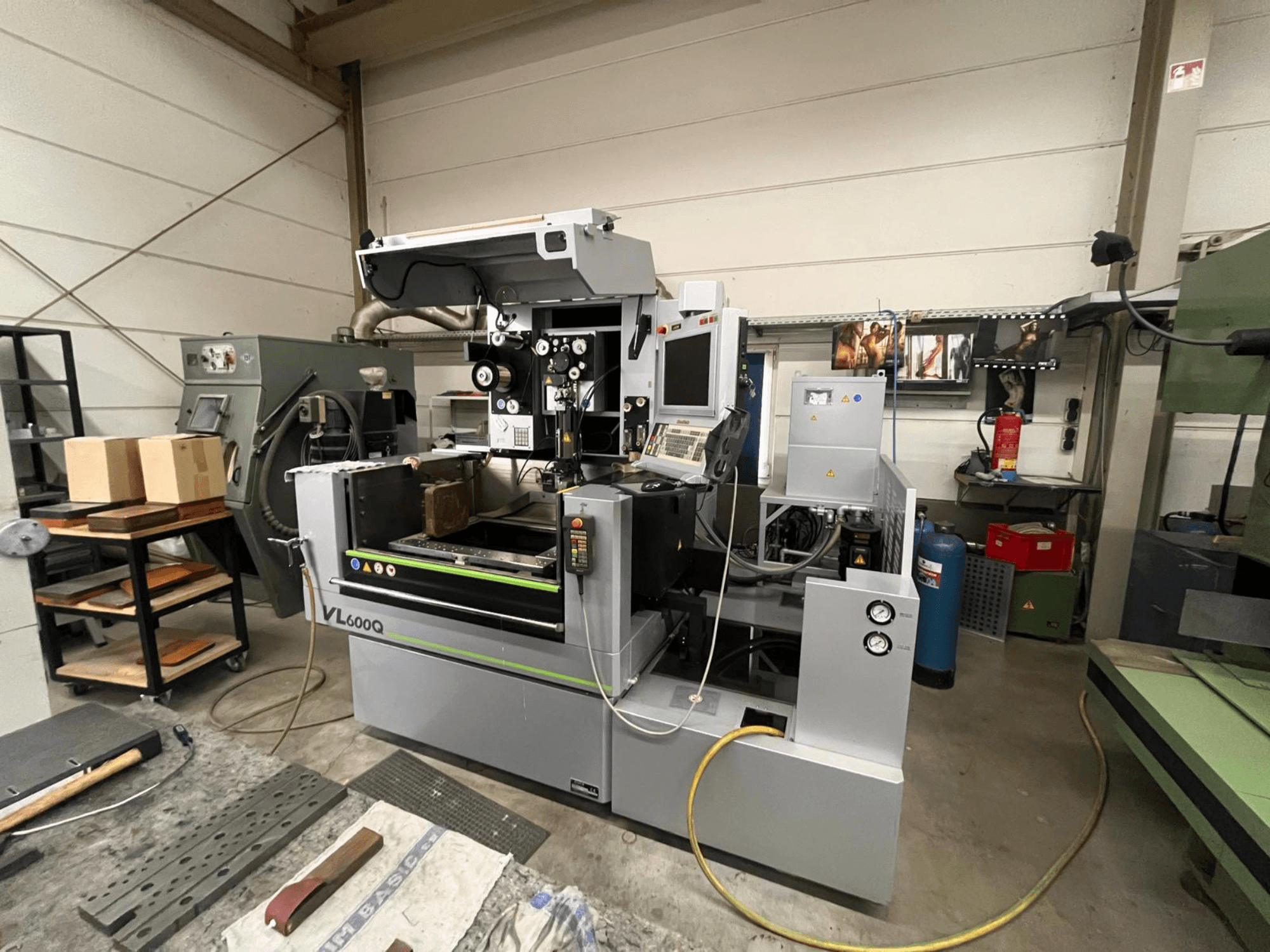 Machine CNC VL600Q dans un atelier, vue de face, avec panneau de commande, matériel en place et divers outils à proximité.