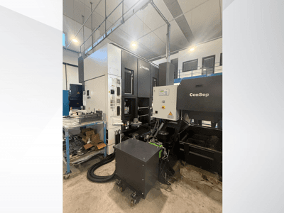 Centre d'usinage Okuma avec unité ConSep, vue latérale, montrant les commandes et l'installation industrielle, y compris le bac à copeaux métalliques.