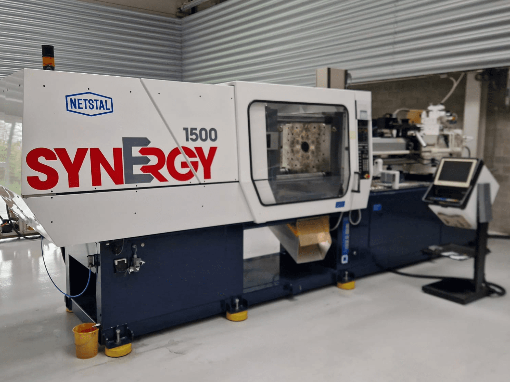 Machine de moulage par injection hydraulique Netstal Synergy 1500-460, vue de face, présentant le panneau de commande et la zone d'injection ouverte.