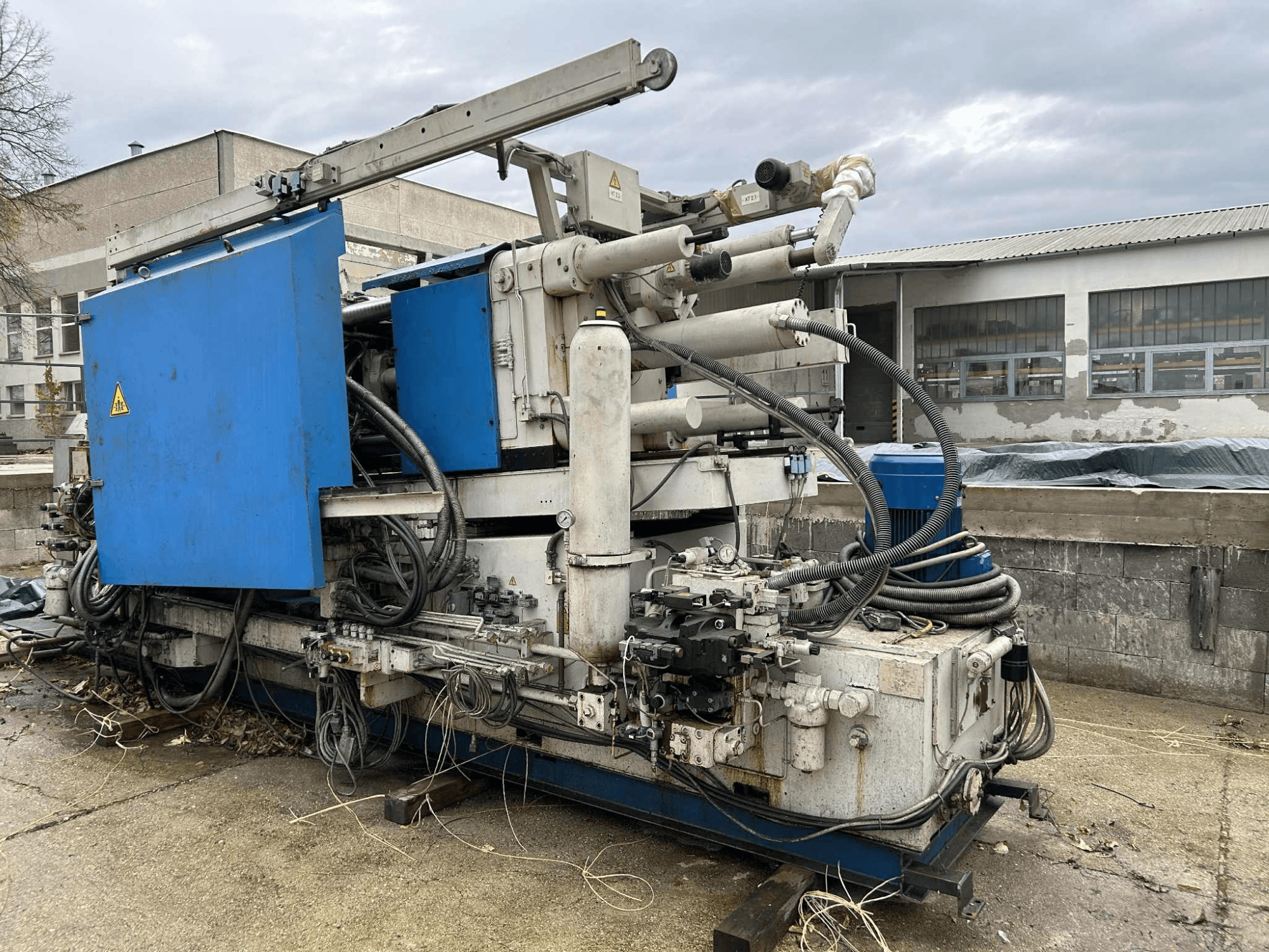 Grande machine hydraulique industrielle avec un carter bleu, divers tuyaux et des composants métalliques, vue de côté.
