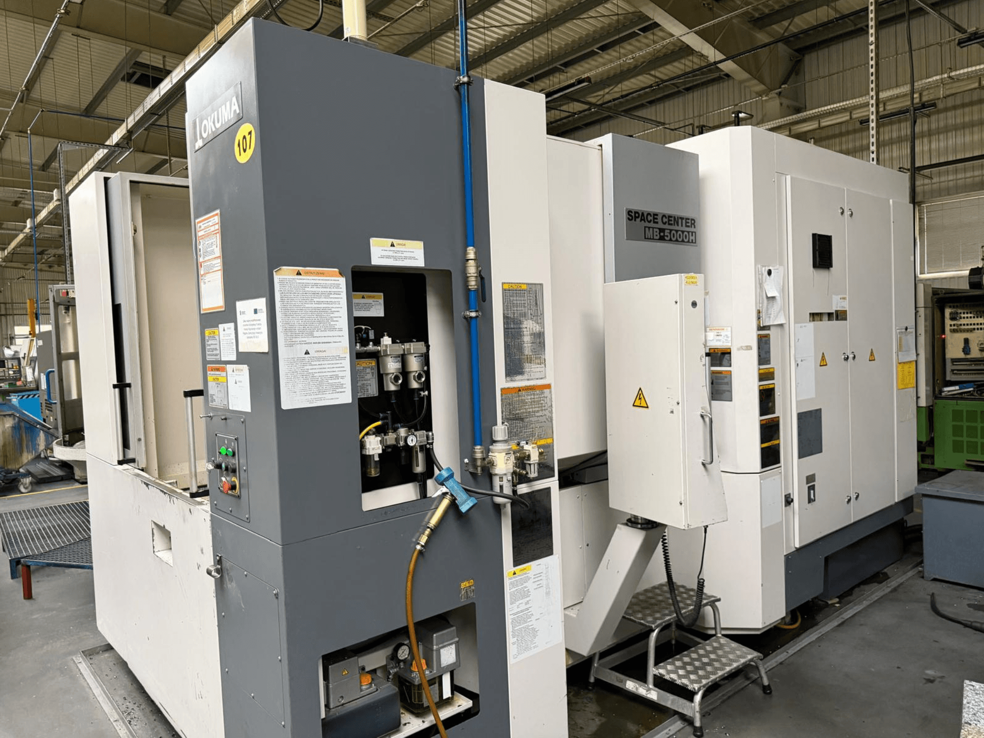Centre d'usinage horizontal Okuma MB 5000H, vue latérale montrant le panneau de commande et les composants de la machine dans un environnement d'usine.