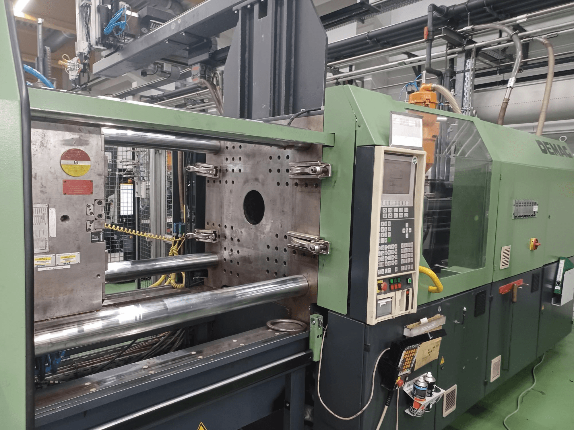 Machine de moulage par injection Demag, vue de face, avec panneau de commande, vérins hydrauliques métalliques et dispositifs de sécurité.