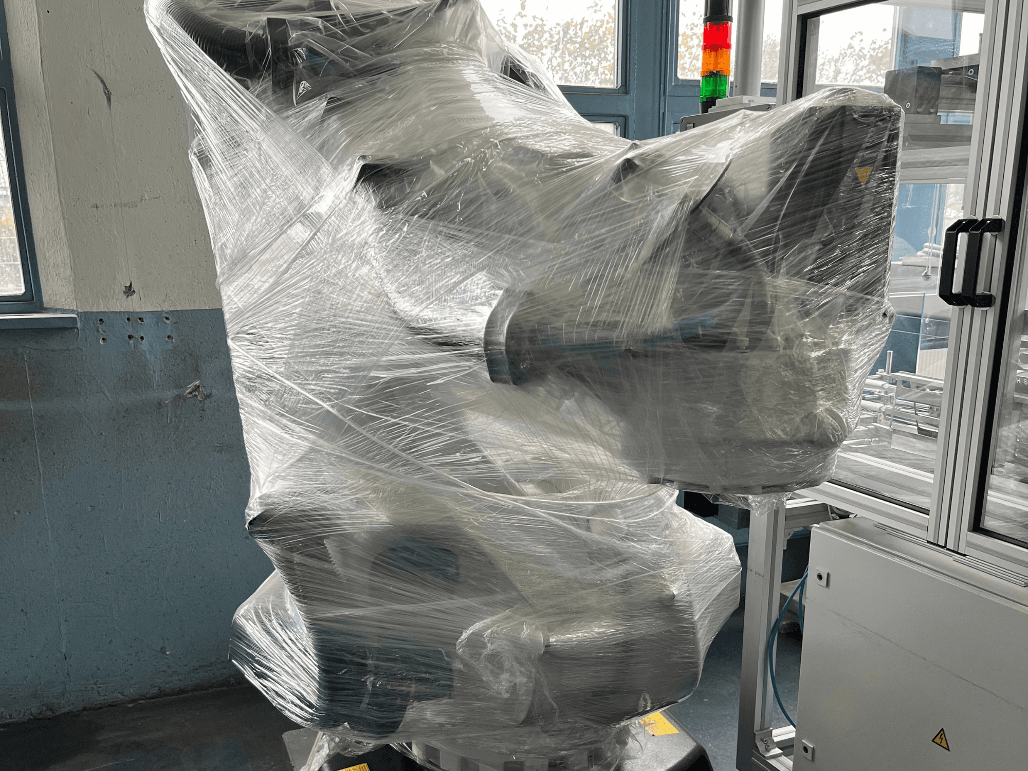 Bras robotique industriel enveloppé de plastique, vue de face. Comprend l'unité de commande et le voyant lumineux. Marque non visible.