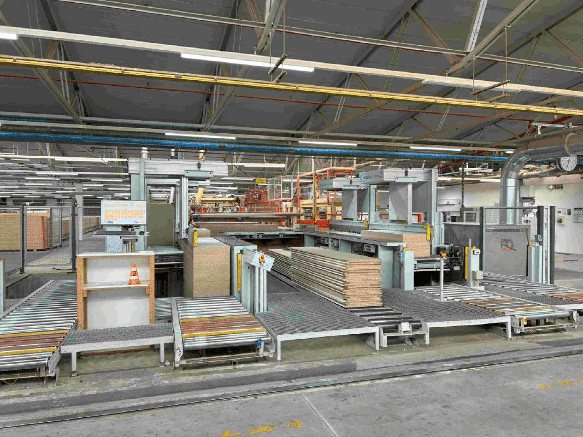 Intérieur d'une usine de fabrication montrant des chaînes de montage avec des panneaux empilés et des machines, vue de face, lumière vive, équipement moderne.