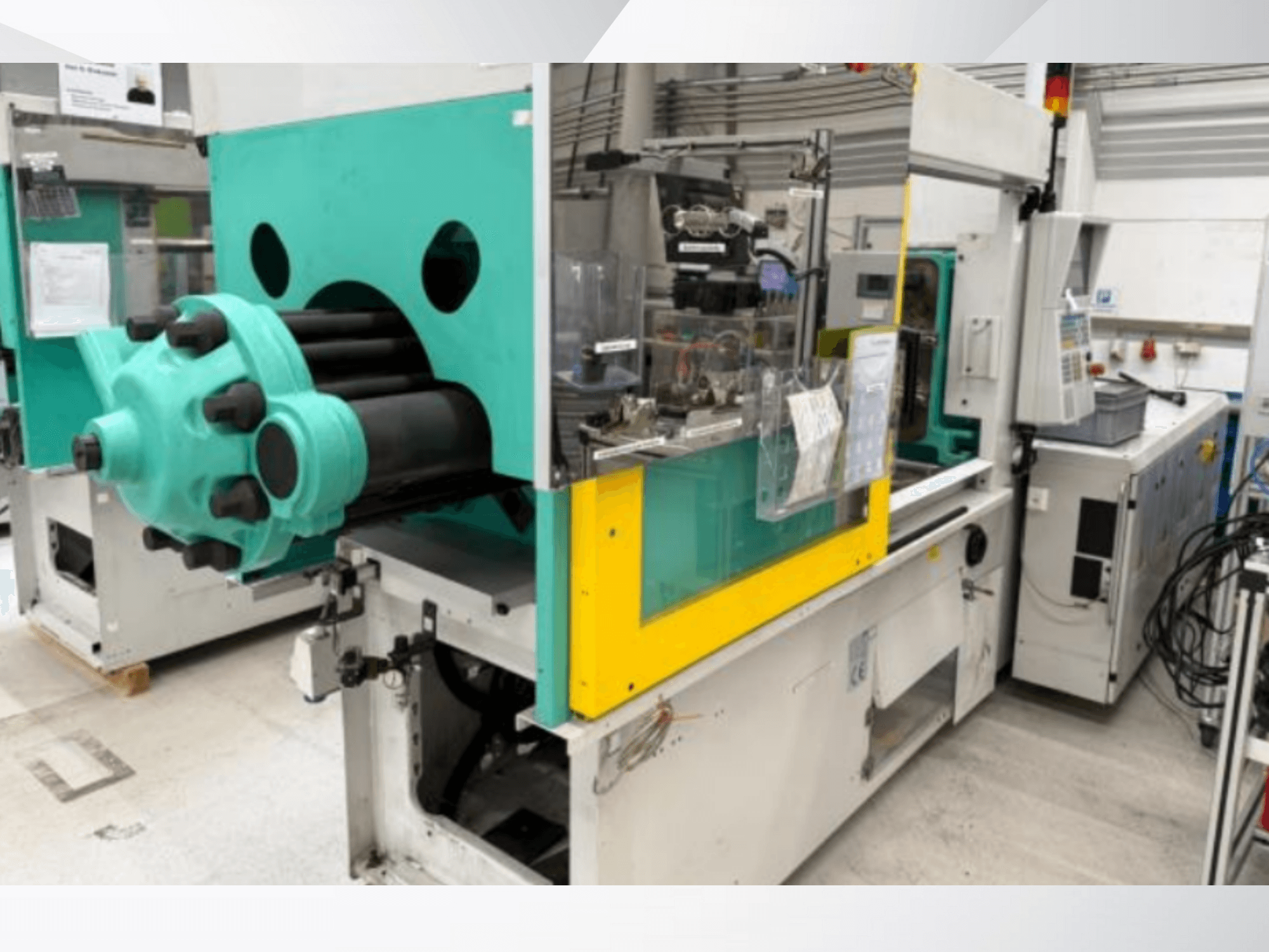 Machine de moulage par injection, bleu clair et jaune, vue de face, comportant un moule visible et un panneau de commande avec des étiquettes.