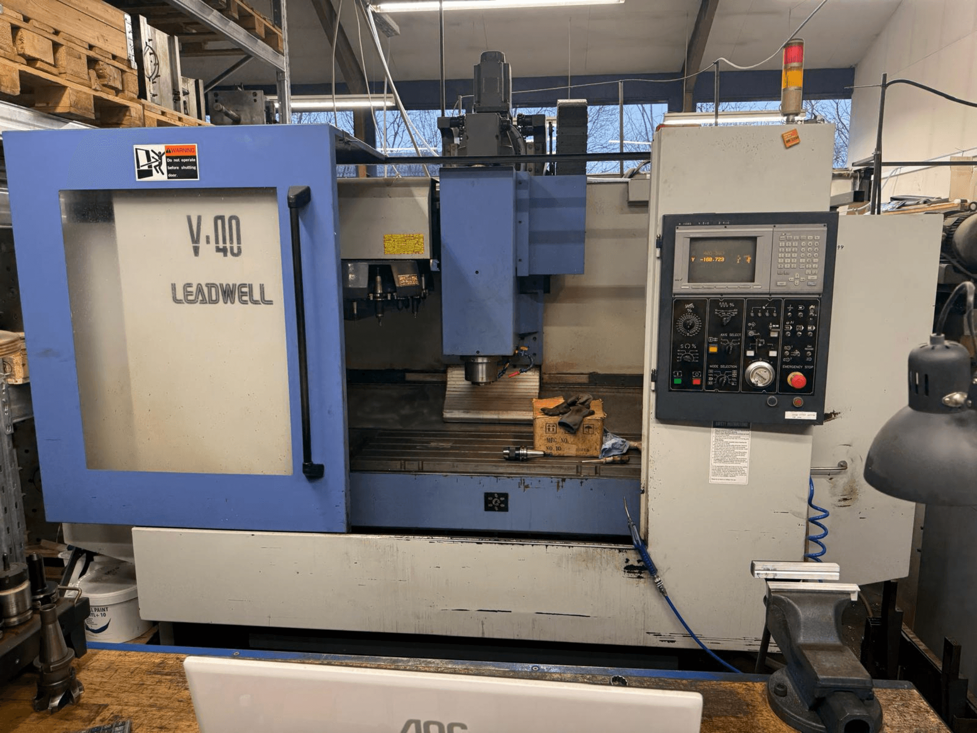 Fraiseuse LEADWELL V-40 CNC, vue de face, comprenant un panneau de commande, des outils de coupe et un étau sur un établi.