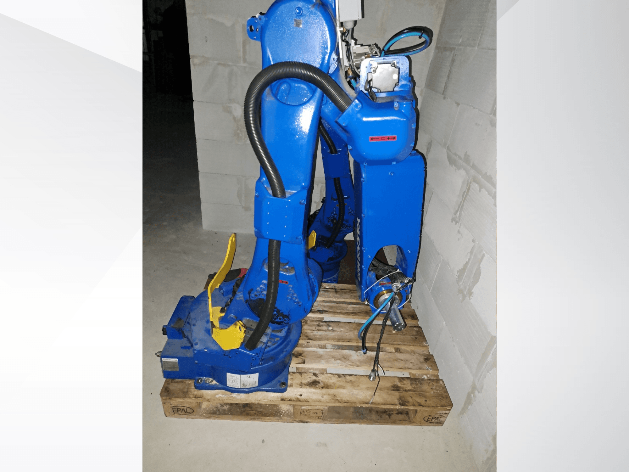 Bras robotisé Yaskawa Motoman GP25 de couleur bleue, vue de profil sur une palette en bois, avec ses câbles et ses articulations mécaniques.