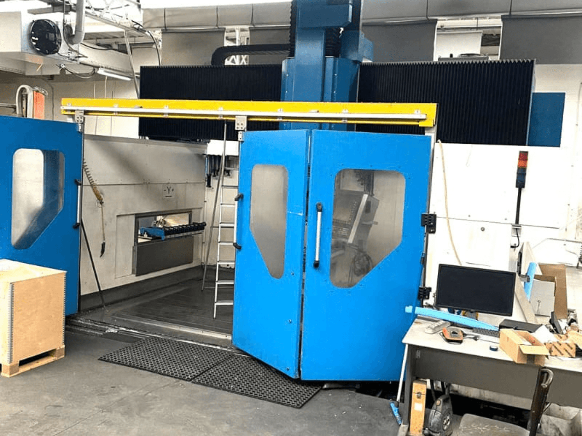 Vue de face du centre d'usinage vertical TECHMILL LABOR SHAPE 3220, dont les portes bleues sont ouvertes, dévoilant ainsi la zone de travail à l'intérieur.