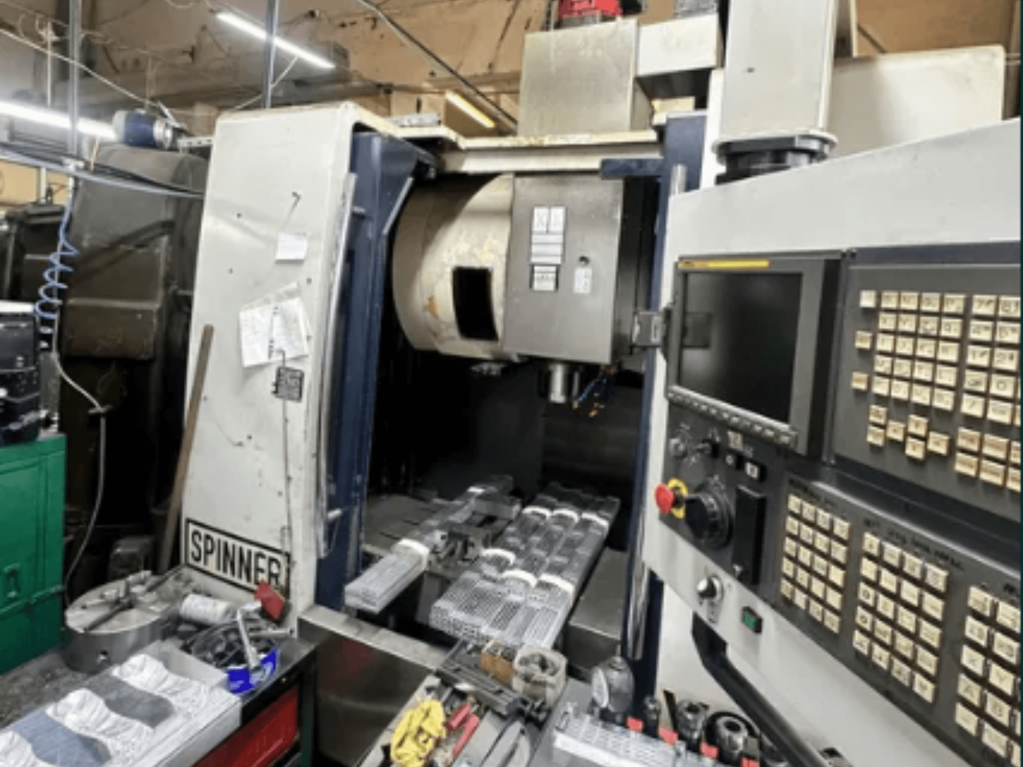 Machine CNC de Spinner, vue de face ; elle comporte une interface à écran tactile, des outils sur l'espace de travail et des pièces usinées prêtes à être traitées.