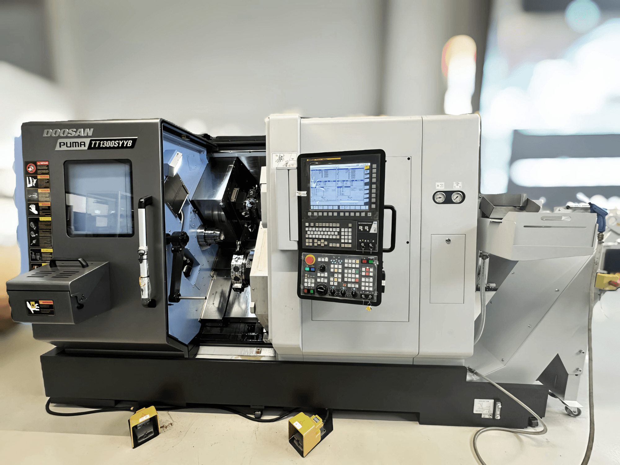 Centre de tournage-fraisage Doosan Puma TT1300SYYB en vue latérale, montrant le panneau de commande et l'intérieur de la machine avec les outils visibles.