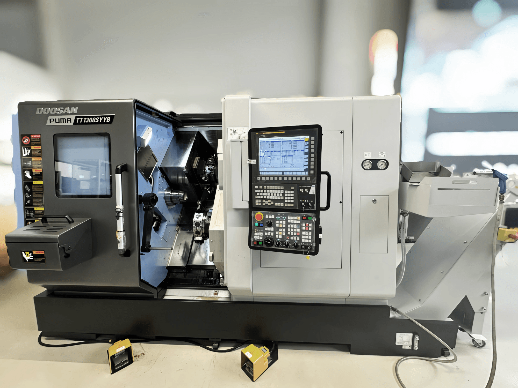 Centre de tournage-fraisage Doosan Puma TT1300SYYB en vue latérale, montrant le panneau de commande et l'intérieur de la machine avec les outils visibles.