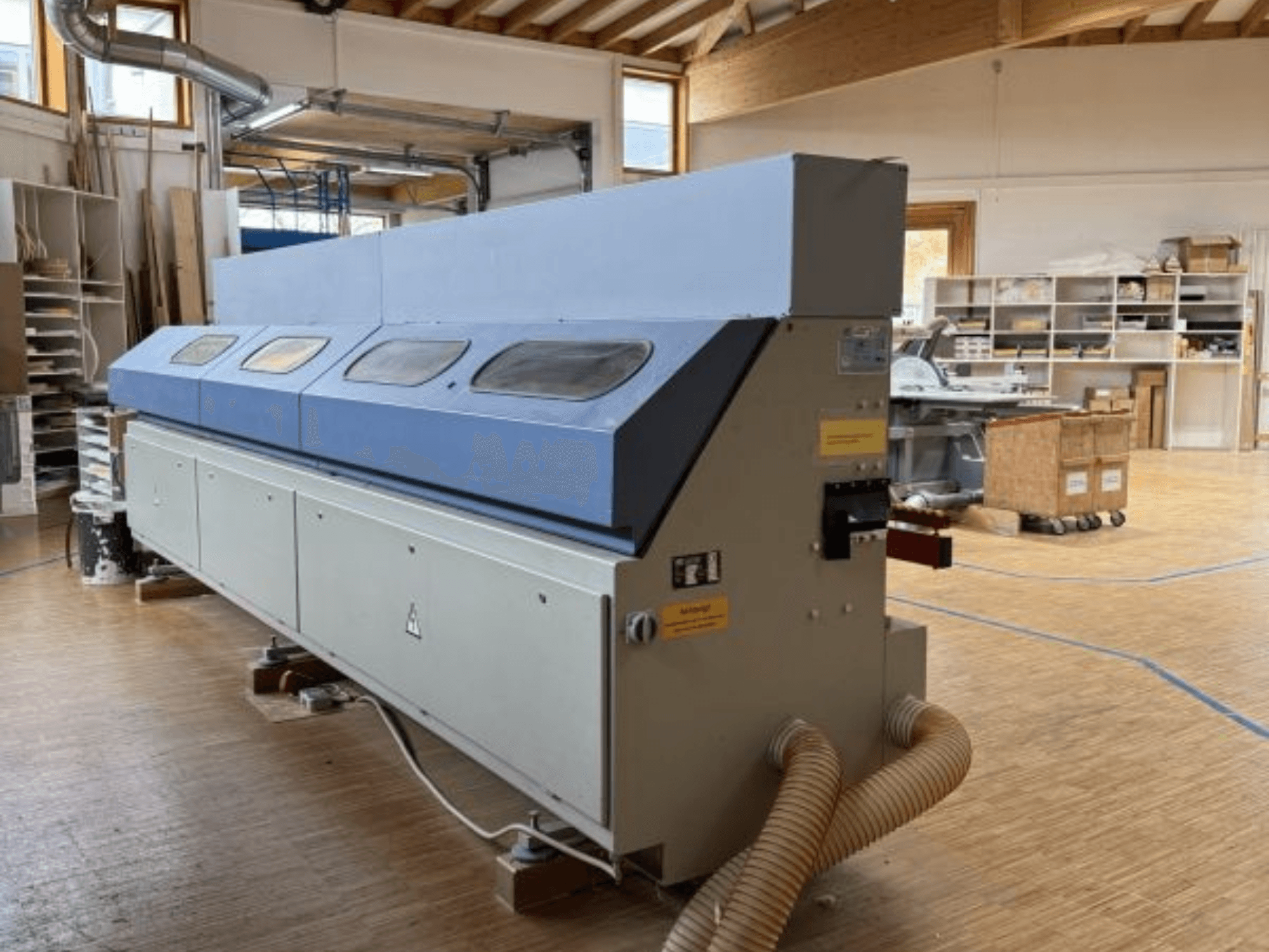 Plaqueuse de chants OTT Pacific V6-F montrée de côté ; elle est dotée d'un long plateau bleu et d'un panneau de commande avec fixation pour le tuyau d'arrosage.