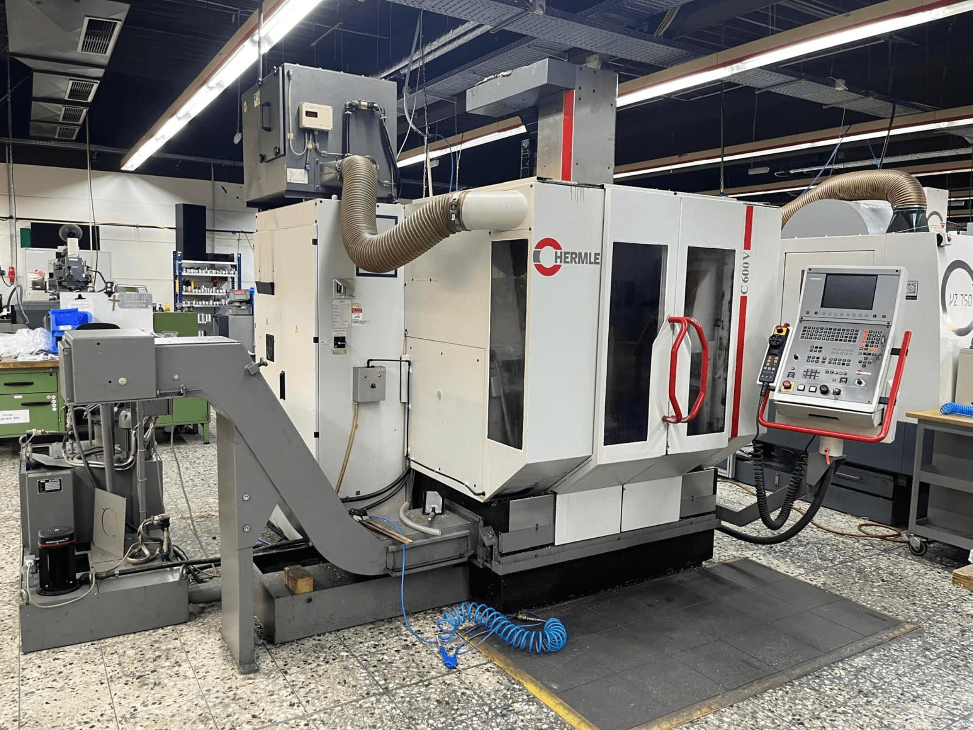 Centre d'usinage vertical HERMLE C 600 V dans un atelier, vue de face montrant le panneau de commande et les dispositifs de ventilation.