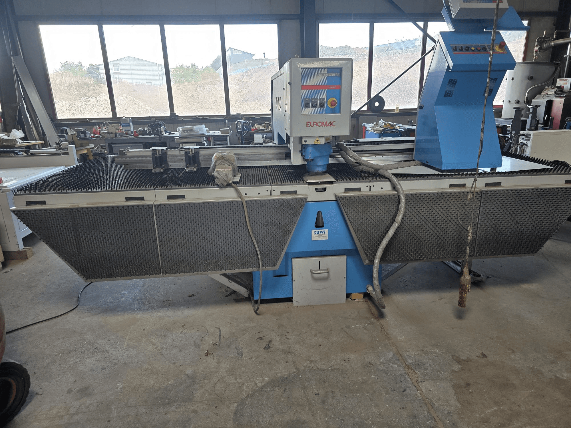 Poinçonneuse CNC Euromac BX 1250/30 dans un atelier, vue de profil mettant en valeur les commandes de la machine, son design industriel et son plateau de découpe métallique.