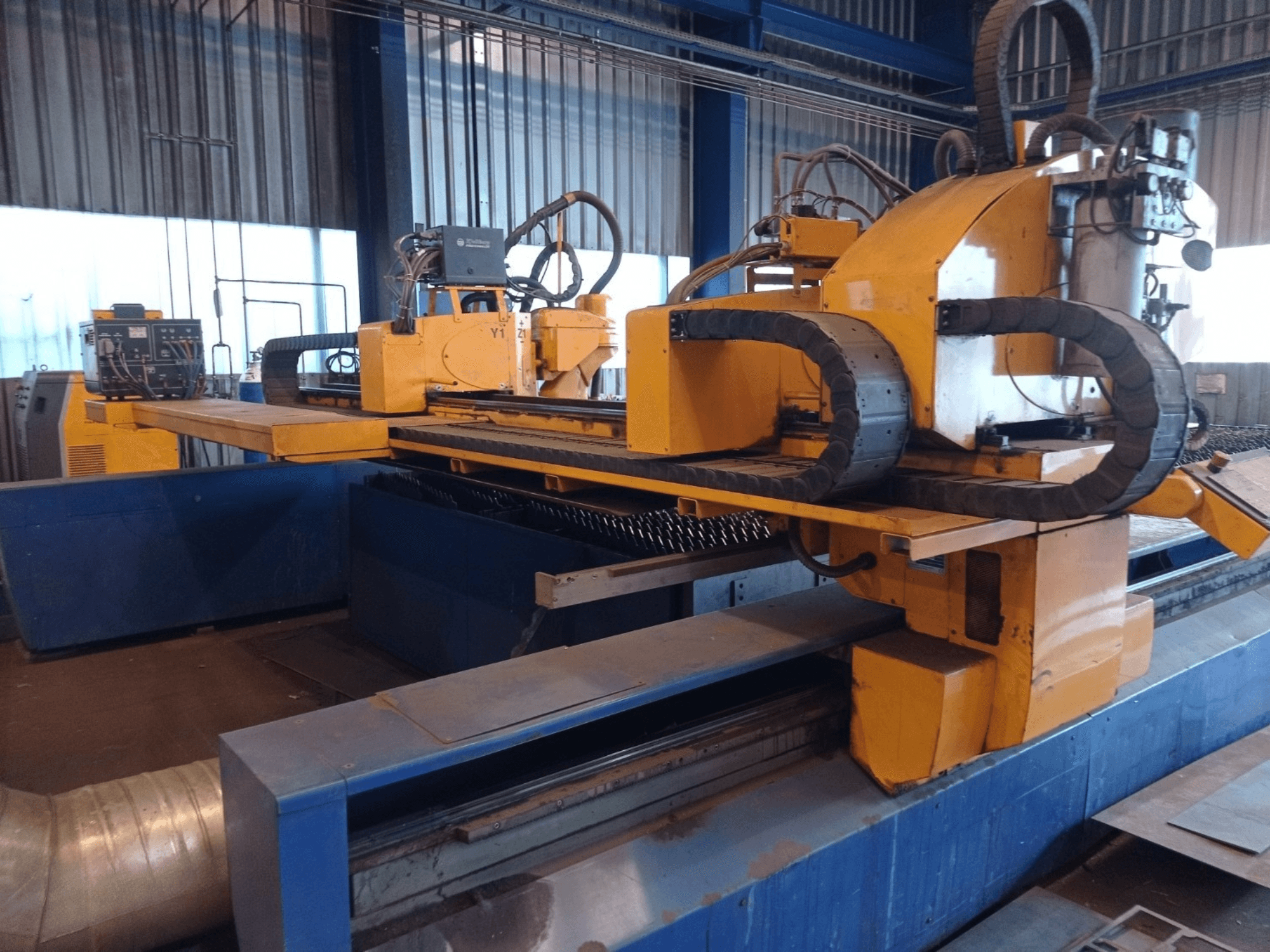 Machine de découpe plasma CNC jaune avec deux bras horizontaux, présentée de face, avec panneau de commande et banc de découpe.