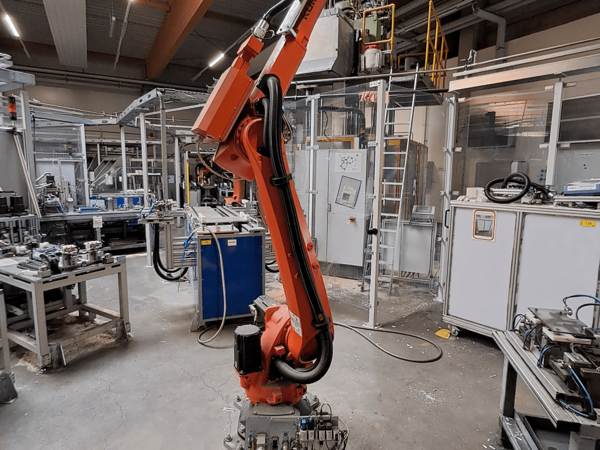 Bras robotisé KUKA KR 26 R3100/SEL dans un environnement industriel, vu de profil avec des équipements en fonctionnement à l'arrière-plan.