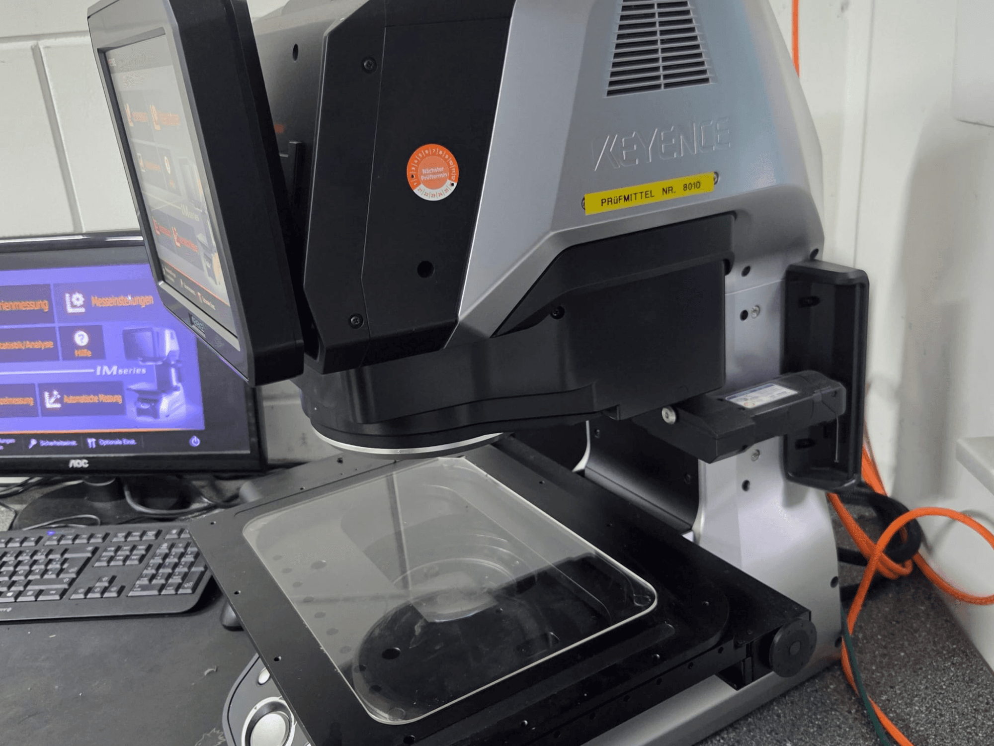Machine de mesure optique KEYENCE IM 7030, vue de face avec écran tactile et plaque de mesure en verre.