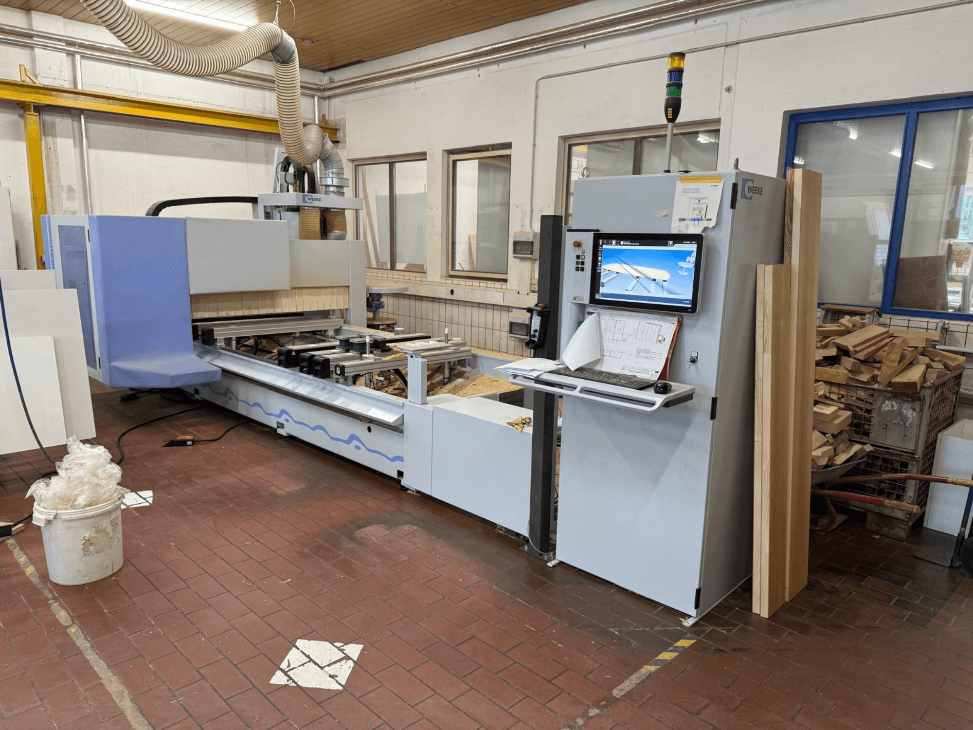 Centre d'usinage CNC pour le bois Weeke PROFI BMG211/32/12/K, vue de face, avec panneau de commande et pièces en bois, équipé d'un système d'aspiration des poussières.
