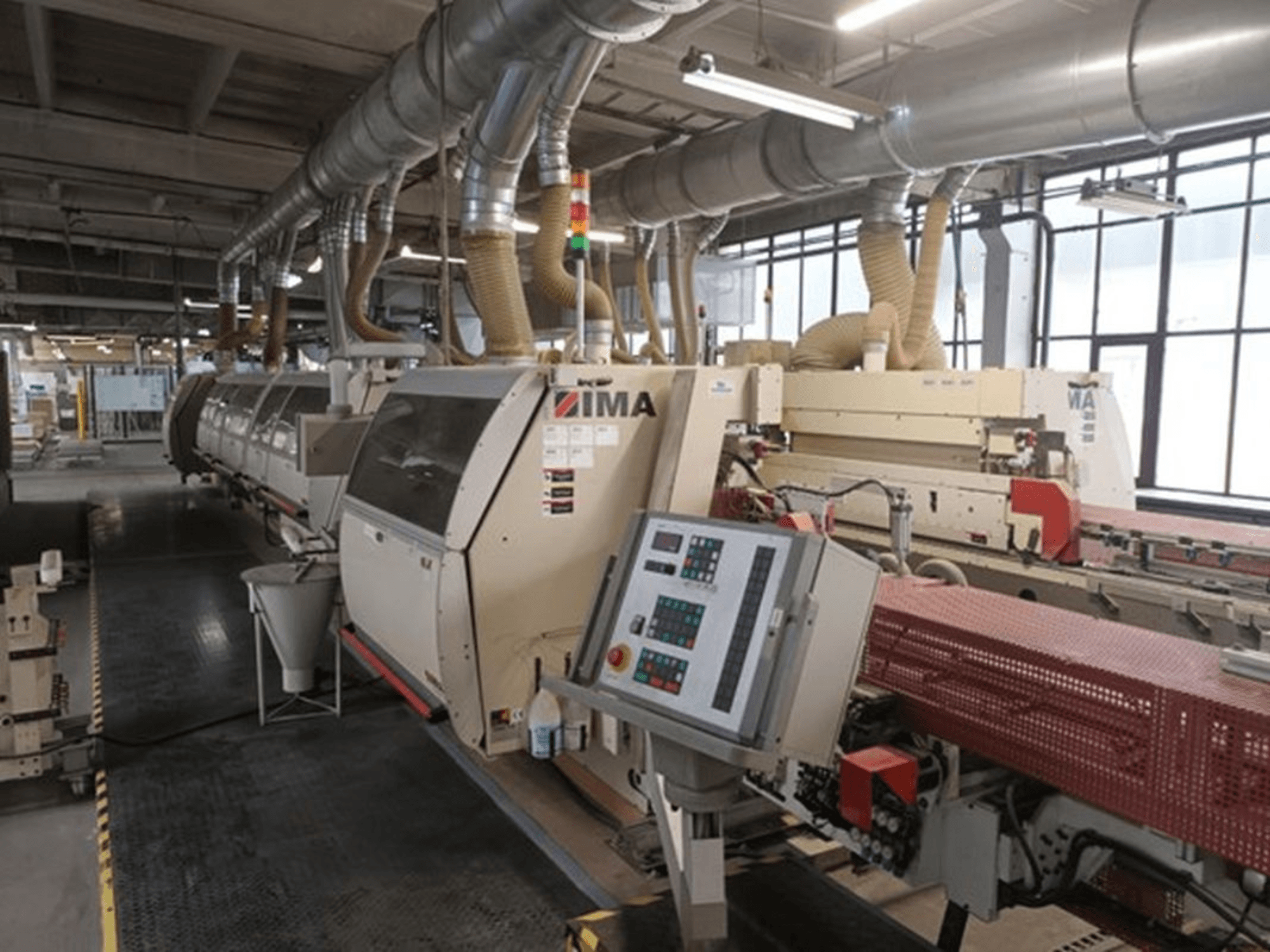 Machines industrielles IMA dans une usine, vue de face, avec panneaux de commande et tuyaux d'extraction de la poussière.