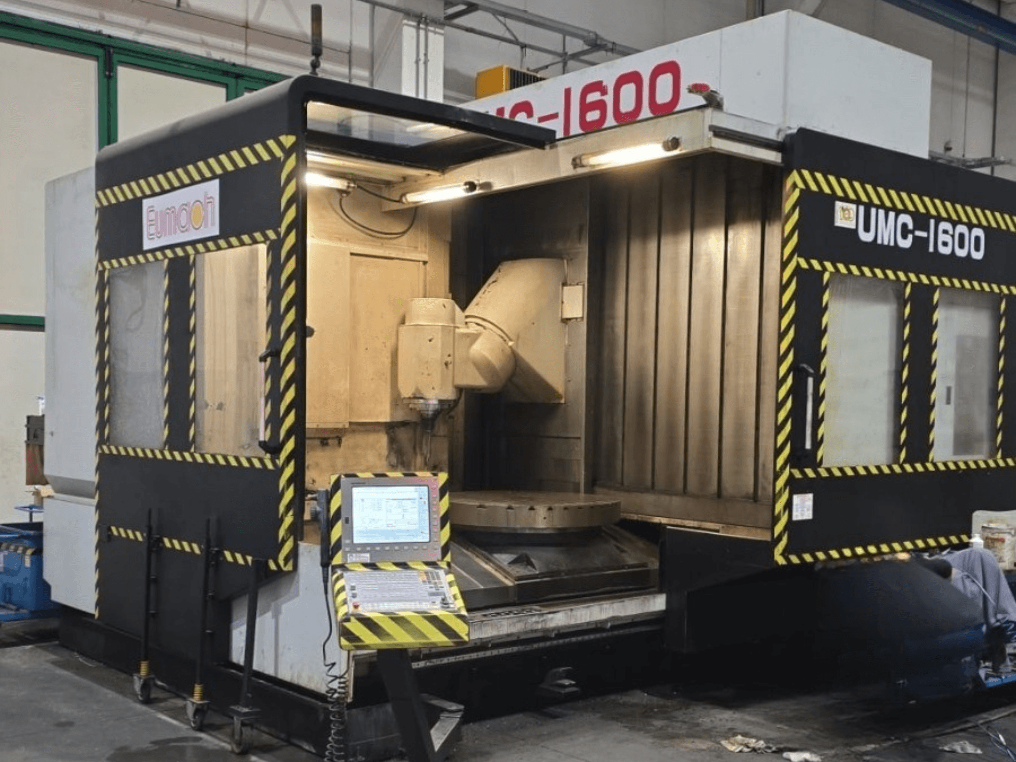 Centre d'usinage vertical Eumach UMC-1600, vue de face montrant les commandes et la zone d'usinage avec les bandes de sécurité.