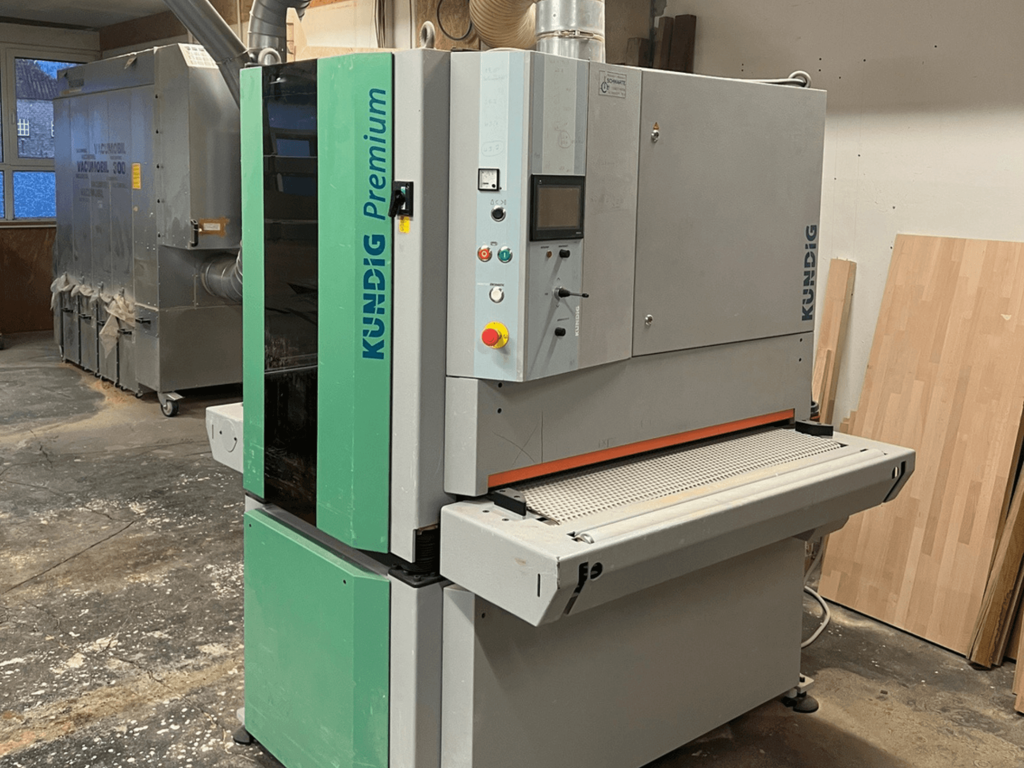 Ponceuse à bande Kundig Premium-1 1100K en gris et vert, vue de côté avec le panneau de commande et la bande abrasive visibles.