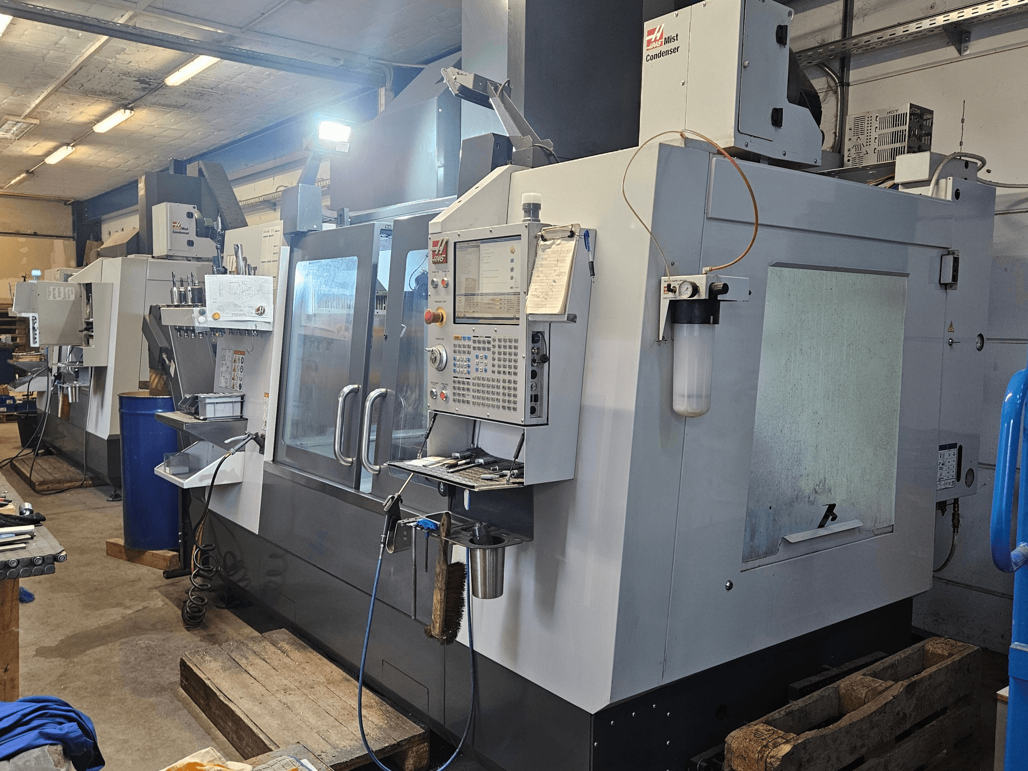 Centre d'usinage vertical Haas VF-3YT/50 dans un atelier, vue de face montrant le panneau de commande, les porte-outils et le condenseur de brouillard.