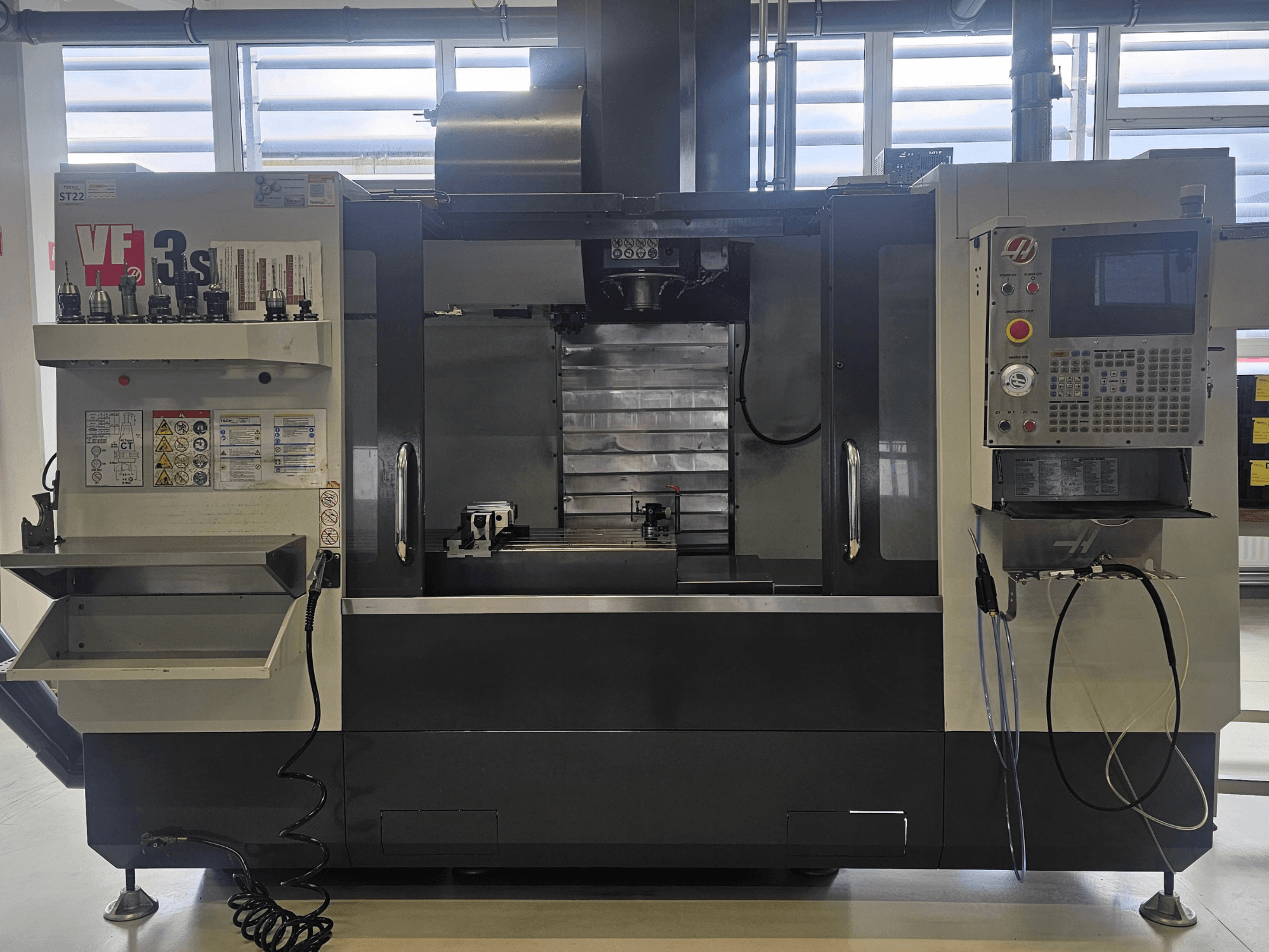 Fraiseuse CNC Haas VF3SS, vue de face, avec les porte-outils, le panneau de commande et le bac à liquide de refroidissement vide, avec les étiquettes de sécurité visibles.