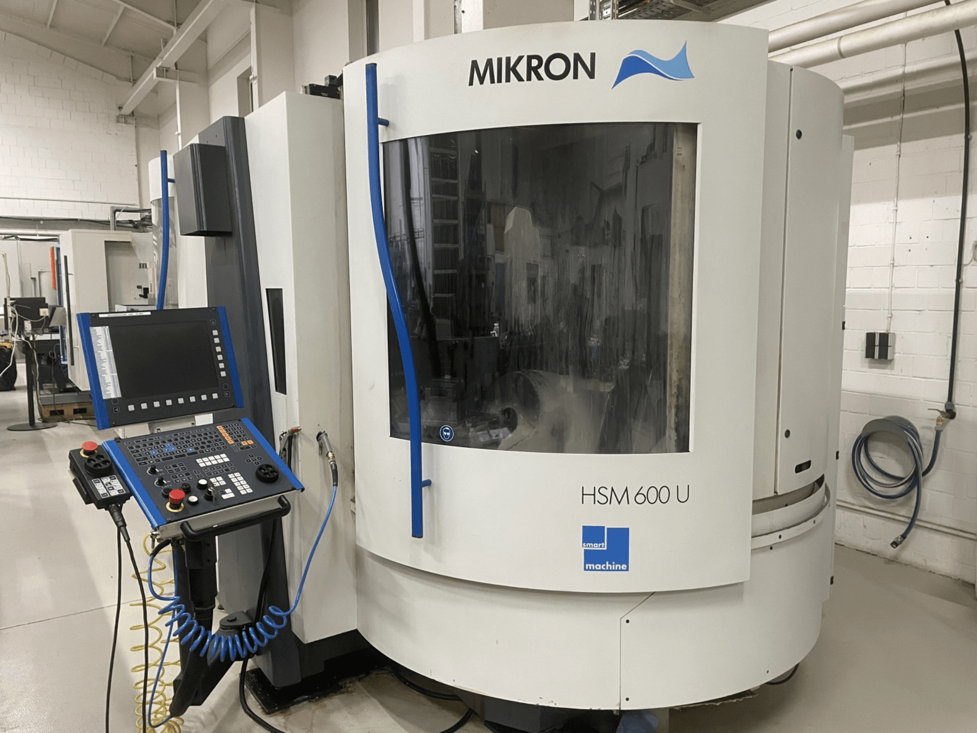 Centre d'usinage vertical MIKRON HSM600U présenté de face, avec un panneau de commande opérationnel et une grande fenêtre de visualisation.