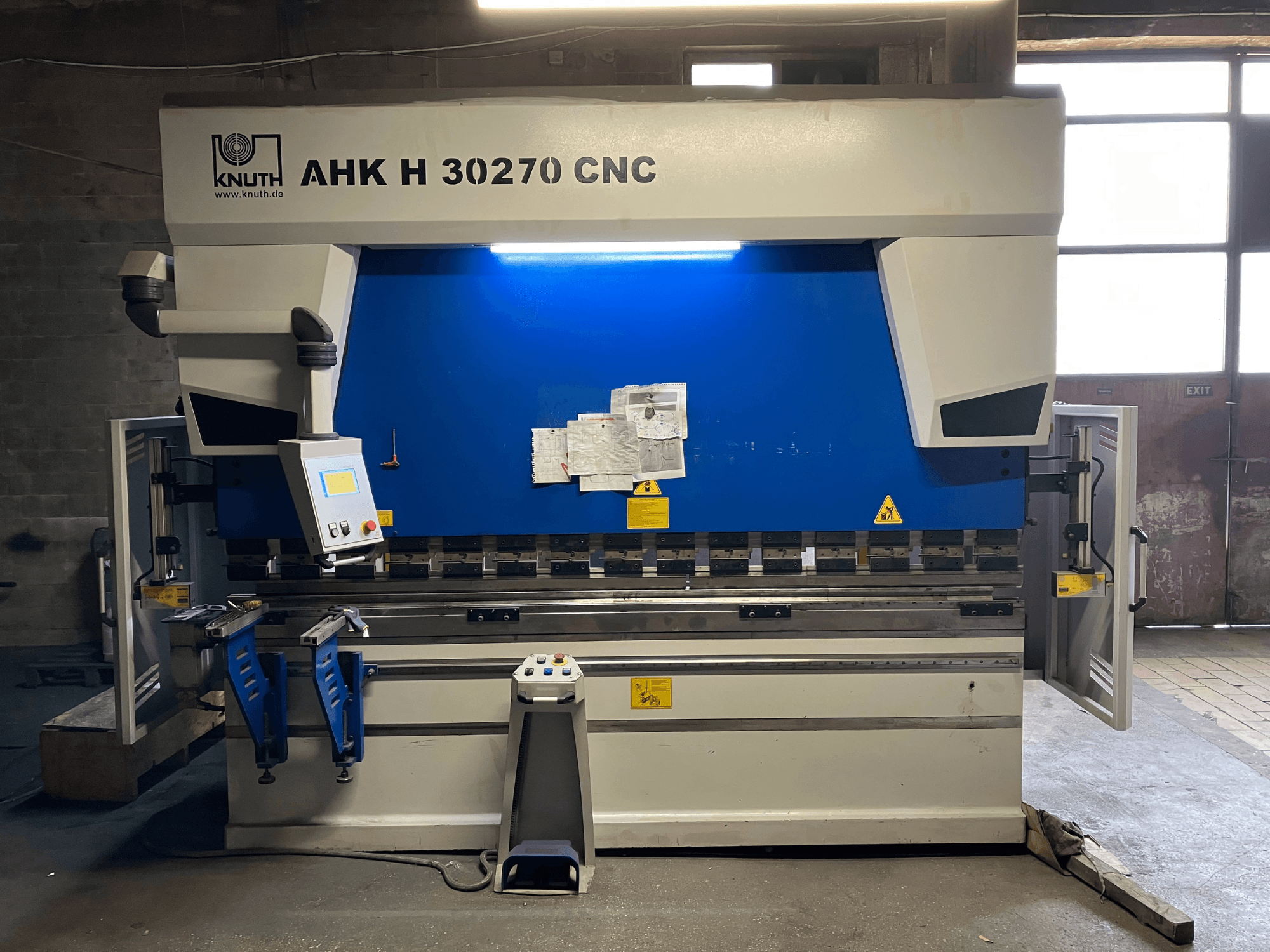 Plieuse CNC KNUTH AHK H 30270 dans un atelier, vue de face, mettant en évidence le panneau de commande et son design bleu et blanc, avec la porte latérale ouverte.