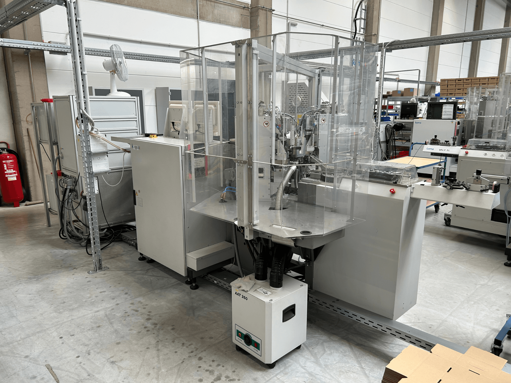 Équipement d'automatisation KOMAX Alpha 433 L dans un environnement industriel. Il est doté d'un capot de sécurité transparent et de divers panneaux de commande.