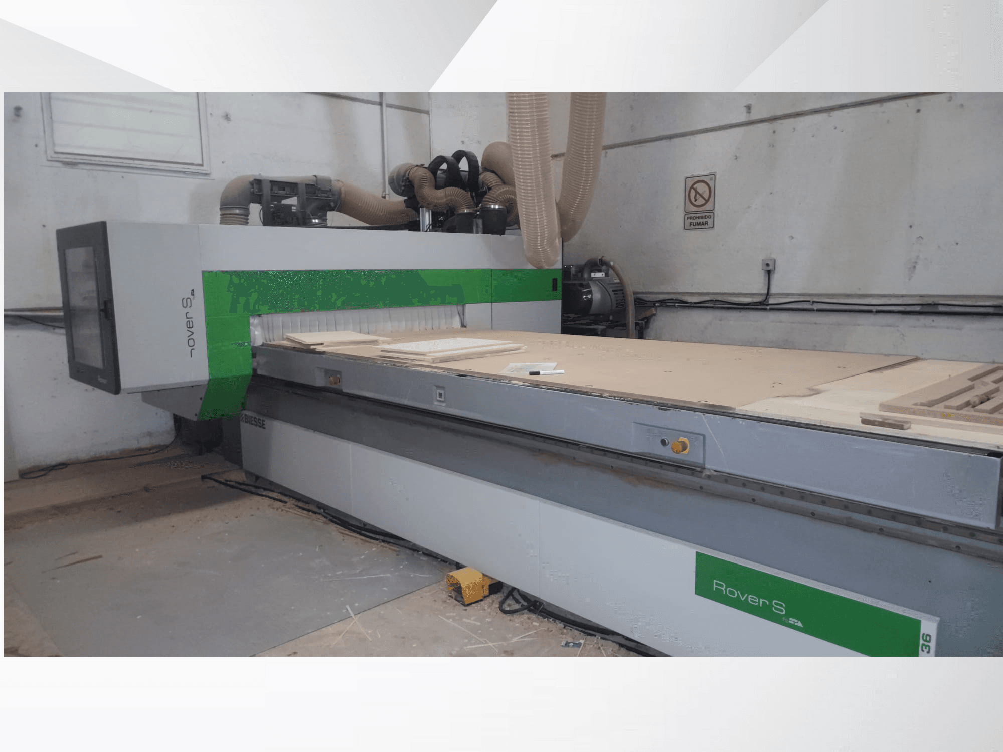 Vue de face de la machine CNC Biesse Rover S, dotée d'une grande surface de travail avec des panneaux en bois et des tuyaux d'extraction de la poussière.