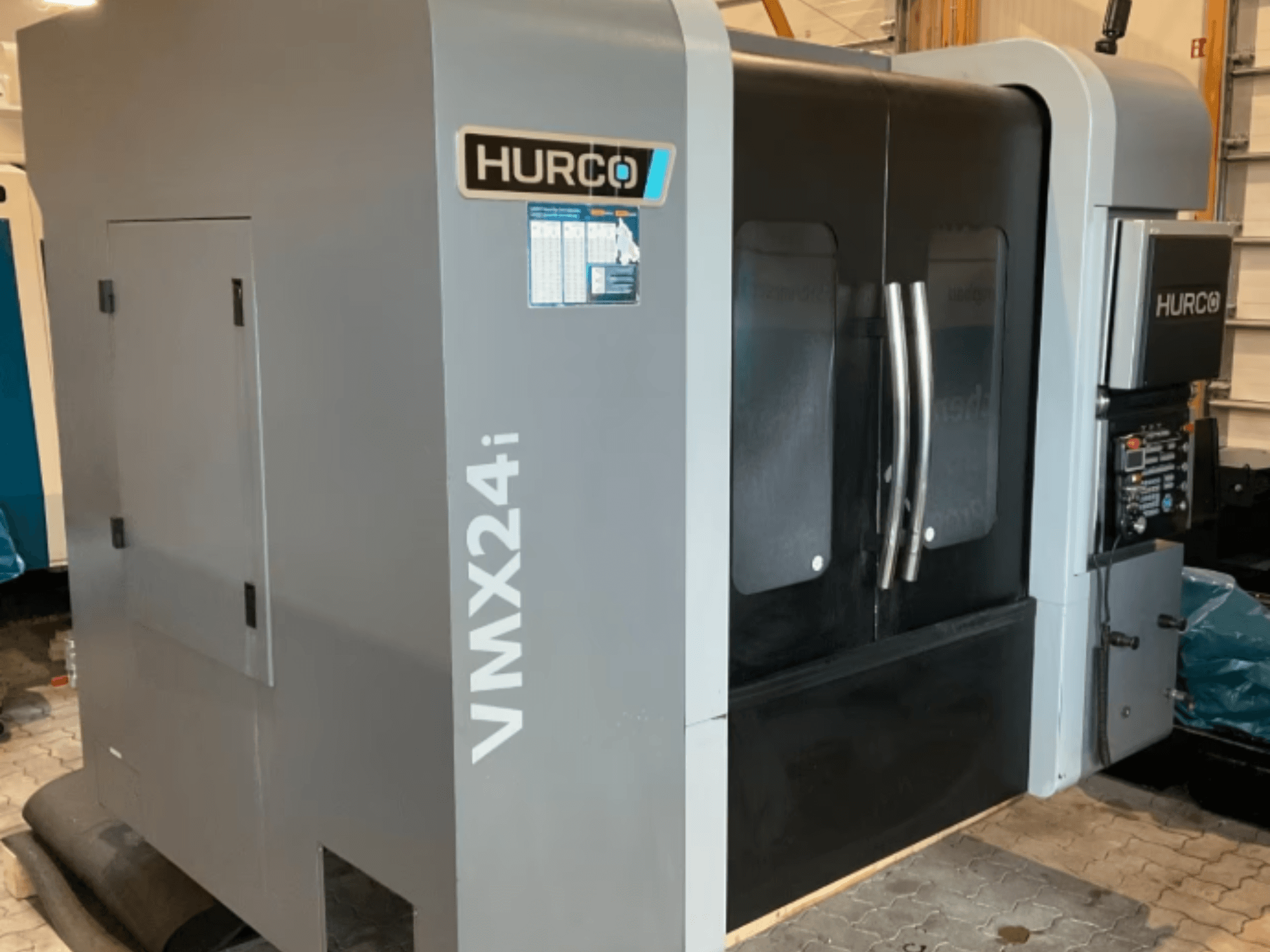 Centre d'usinage vertical Hurco VMX 24i, vue de face avec un châssis gris métallisé, des portes de commande noires et une interface de commande.