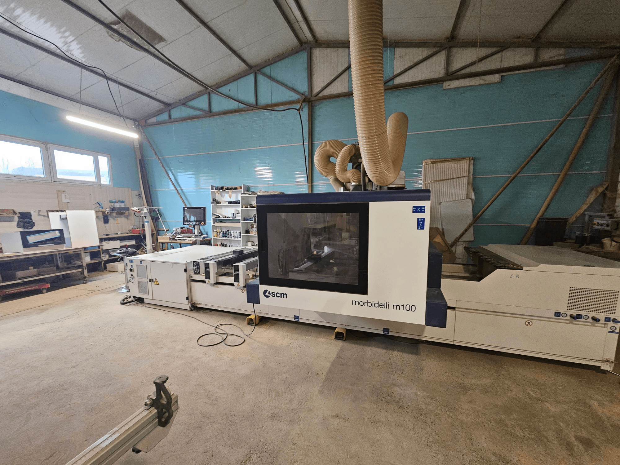 Machine CNC SCM Morbidelli M100 dans un atelier, vue de face, présentant le système d'extraction des poussières et le panneau de commande.