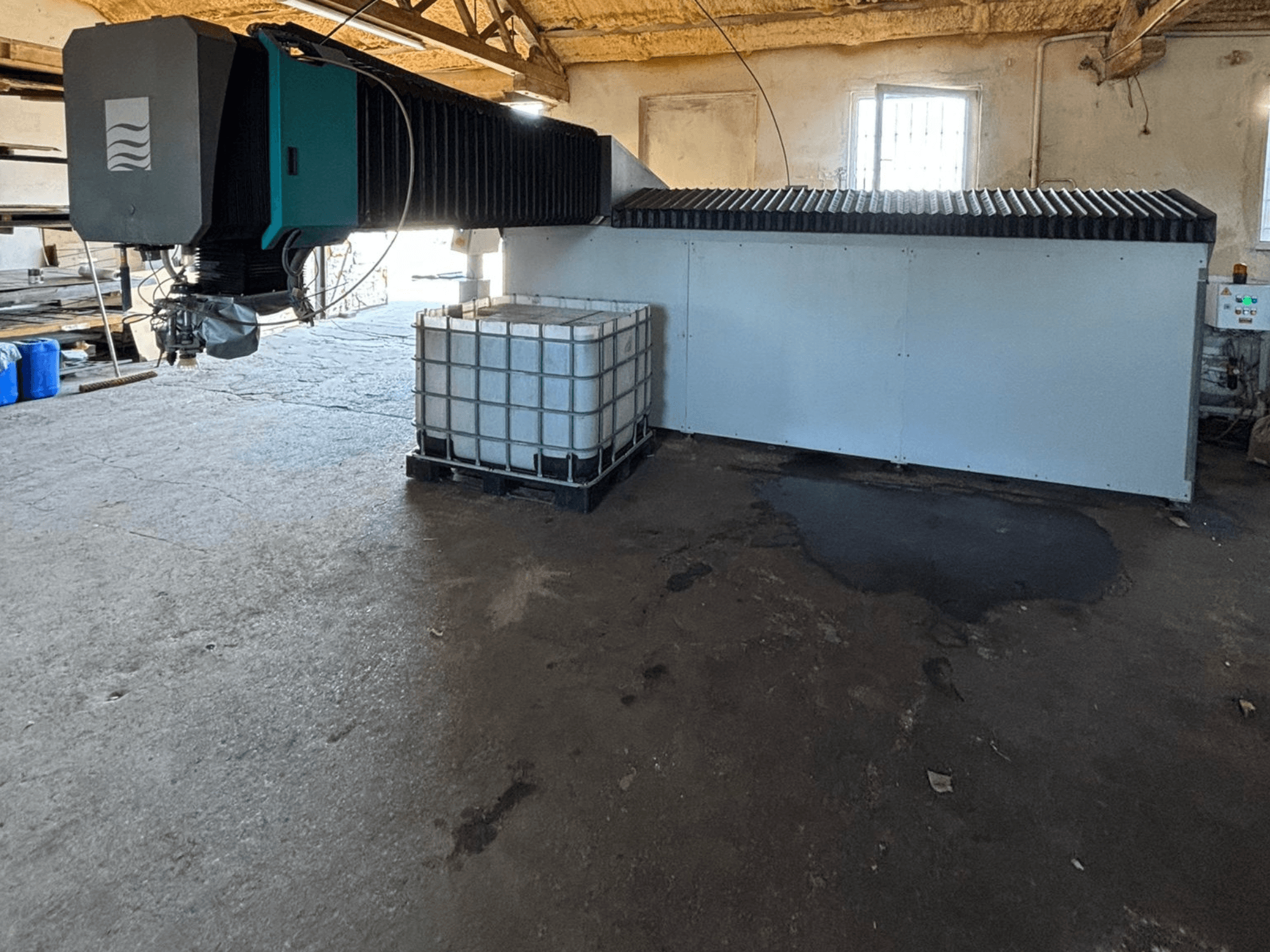 Machine industrielle à jet d'eau dans un atelier, vue de côté, avec un grand réservoir d'eau et un panneau de commande visible à côté.