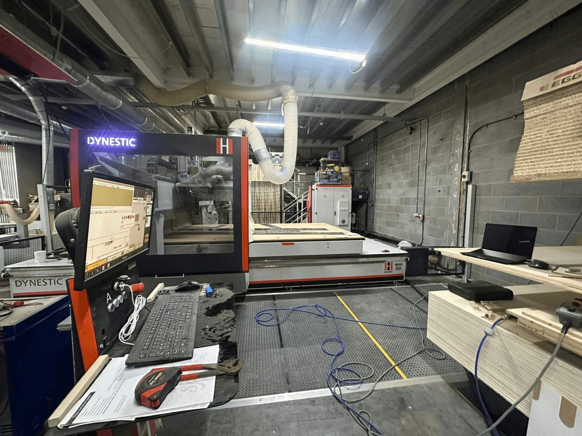 Moulin à bois HOLZHER Dynestic 7535 dans un atelier, montrant le panneau de commande, le moniteur et les matériaux sur la table de travail, vue de face.