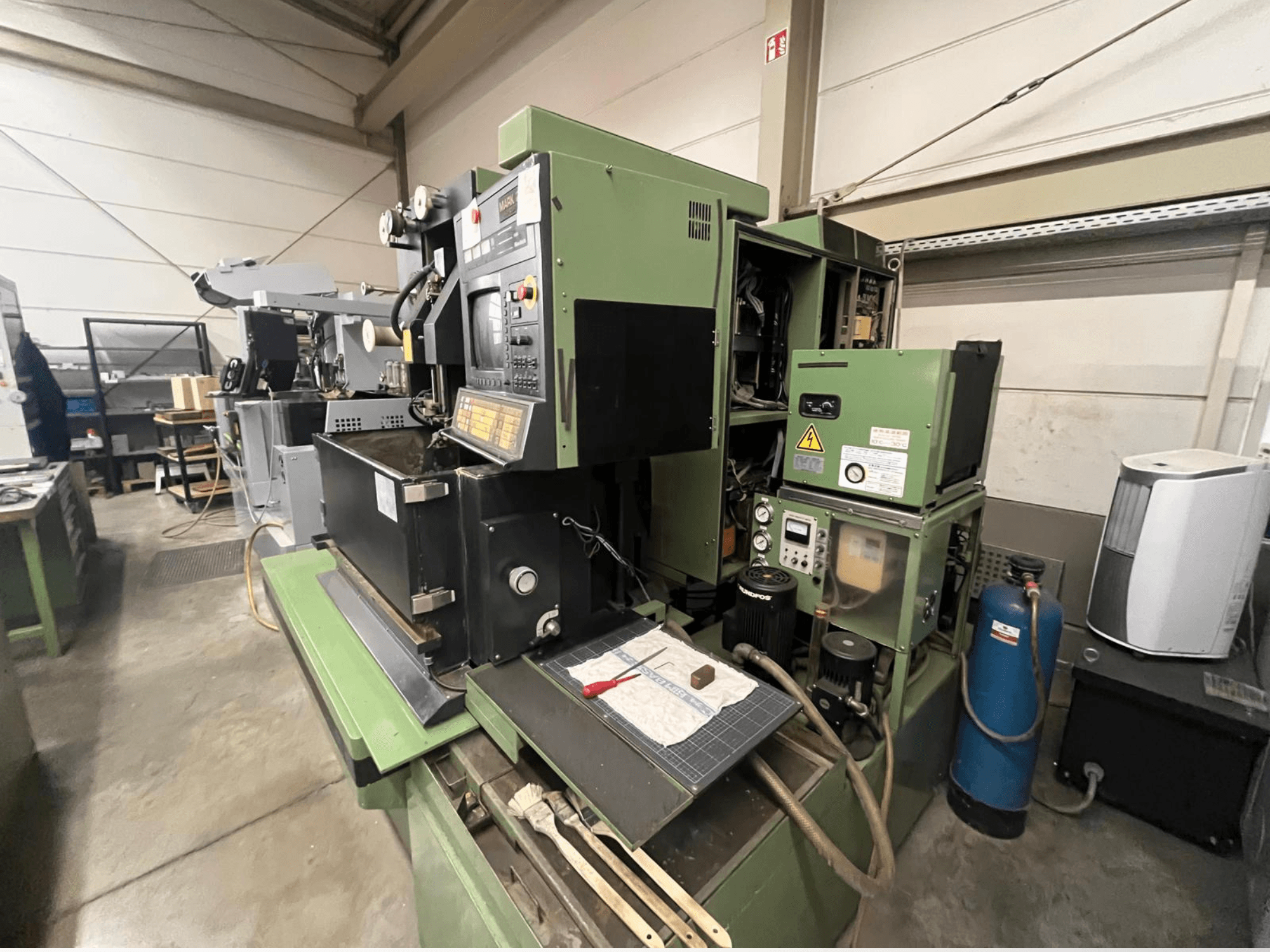 Machine industrielle verte avec panneau de commande, vue latérale ; comprend des composants hydrauliques et une surface de travail avec des outils.