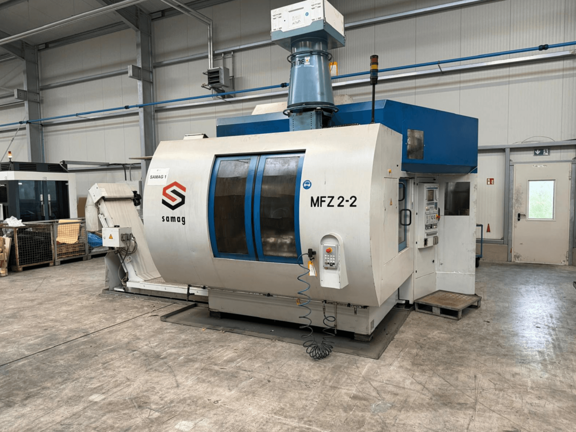 Machine-outil Samag MFZ 2-2, vue de face, montrant le panneau de commande et le couvercle bleu, avec des dispositifs de sécurité dans un environnement industriel.