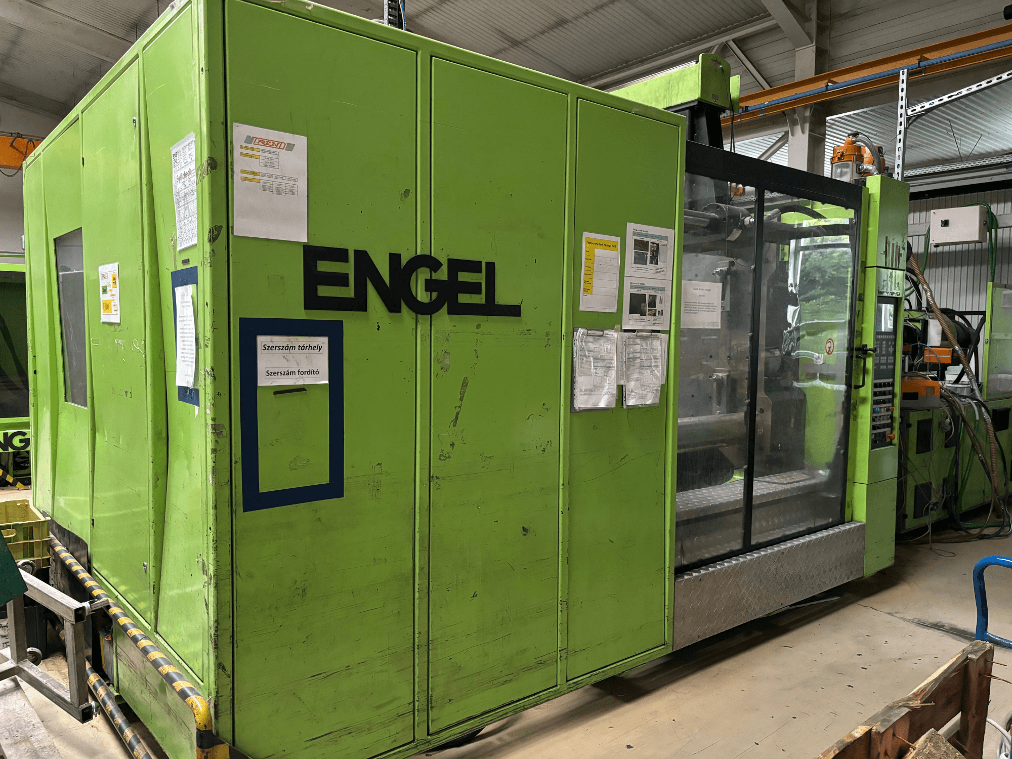 Machine de moulage par injection hydraulique Engel DUO 5550/800, vue de face, avec un extérieur vert et un panneau d'accès transparent.