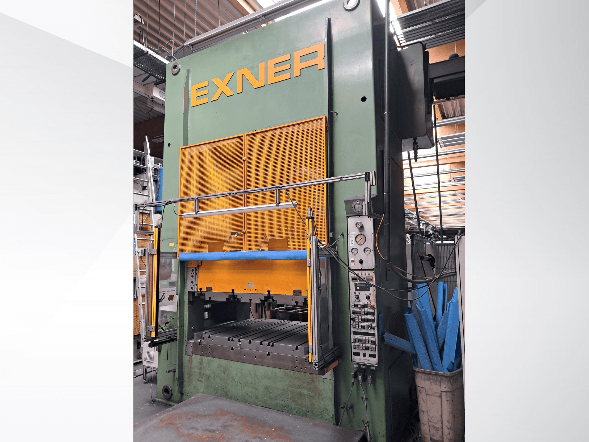 Presse hydraulique EXNER EX SBR 150, vue de face ; avec ses commandes, sa barre de sécurité bleue et sa grille de protection, installée dans un atelier.