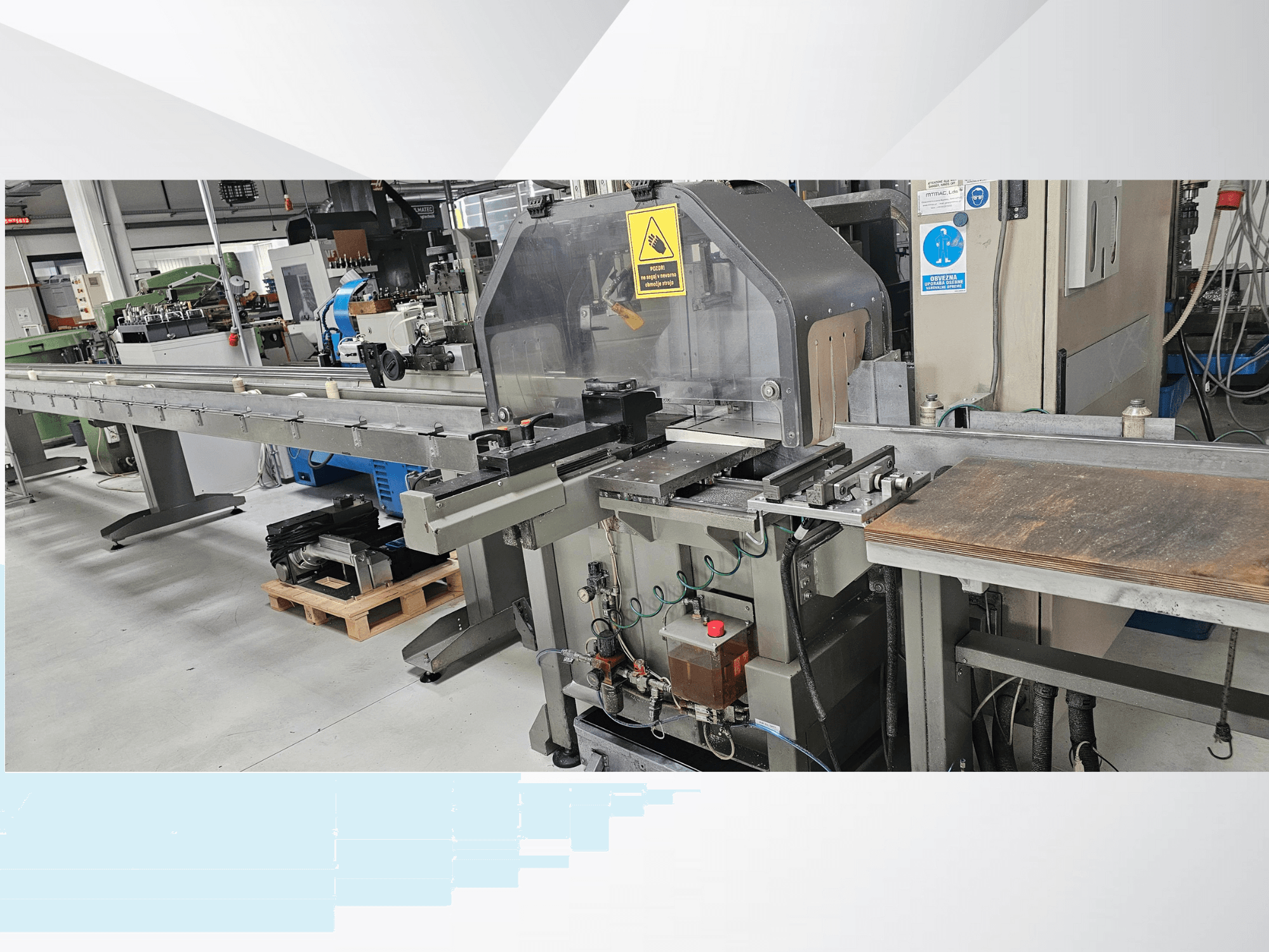 Machine de découpe industrielle vue de côté, avec un long convoyeur, un panneau de commande et des avertissements de sécurité.