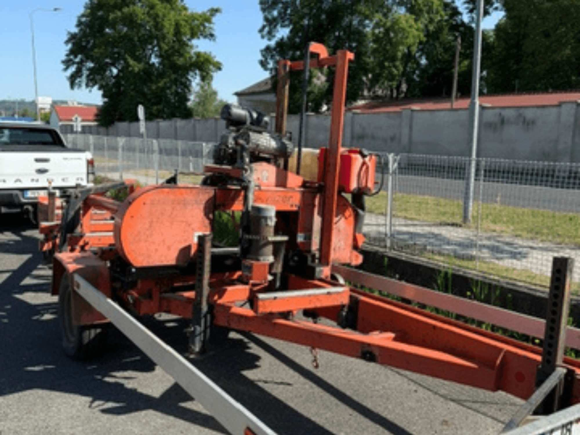 Scie à ruban WOOD-MIZER LT40 de couleur orange, vue de profil sur une remorque, avec les roues et les composants du moteur visibles.