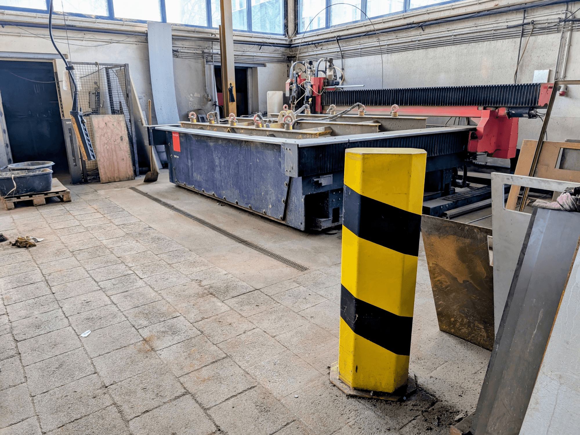 Machine de découpe au jet d'eau Bystronic Byjet L 2030 dans un atelier, vue de côté, avec un poteau de sécurité jaune et des matériaux environnants.