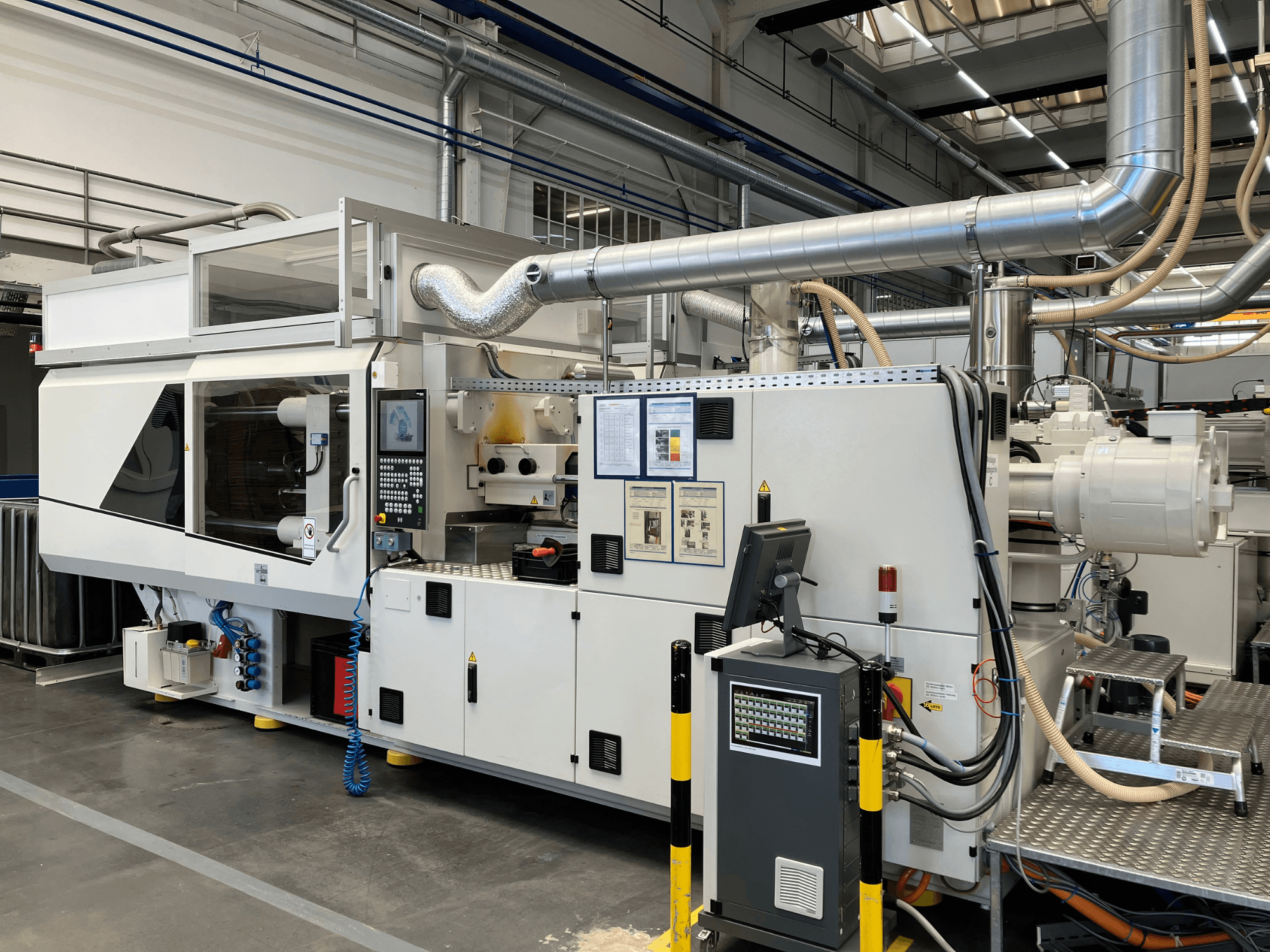 Vue de face d'une machine industrielle avec panneau de commande, tuyaux et écrans d'affichage, présentant un design blanc épuré et des détails techniques.